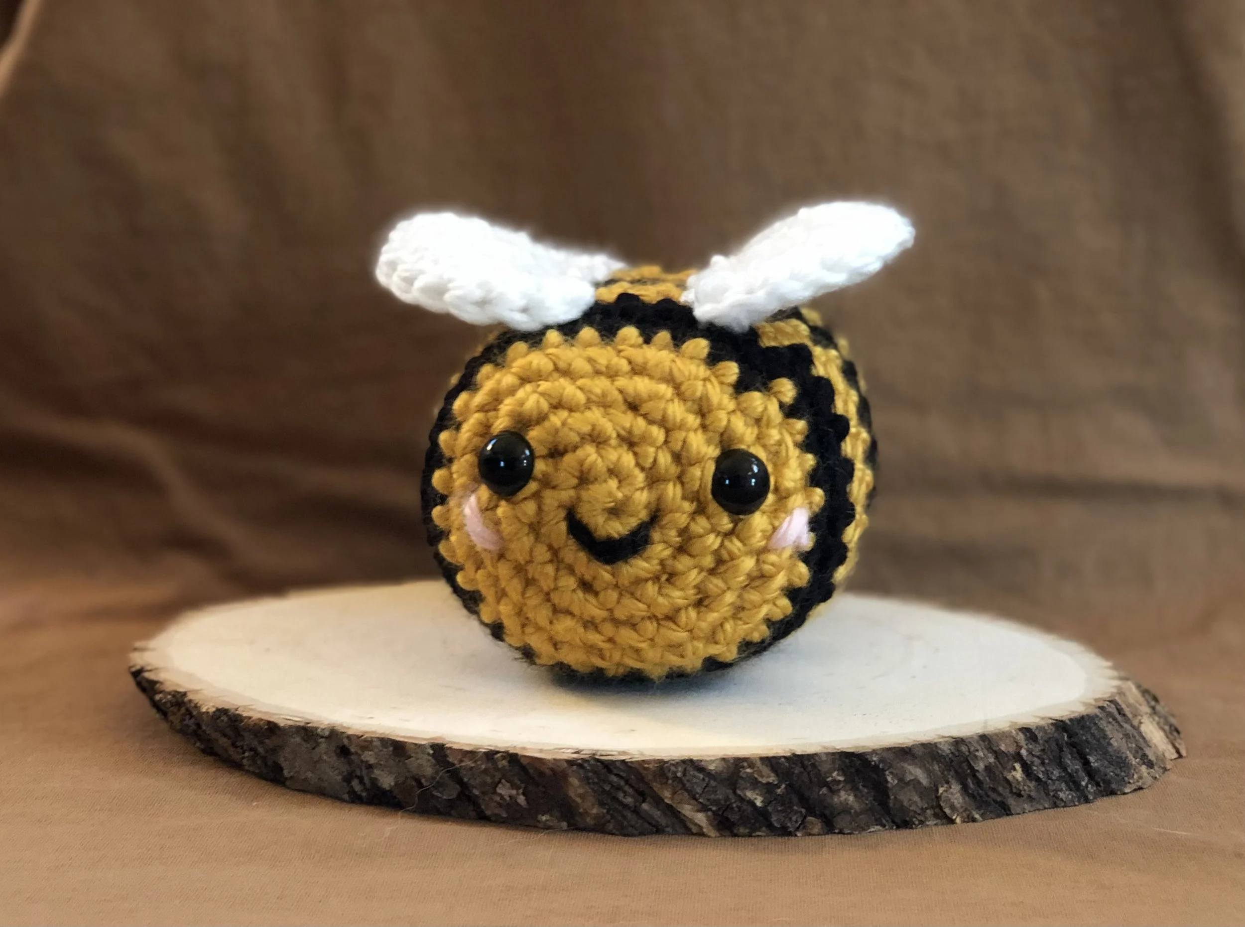 Large crocheted bee. It is yellow with black stripes, white wings, and a small smiley face.