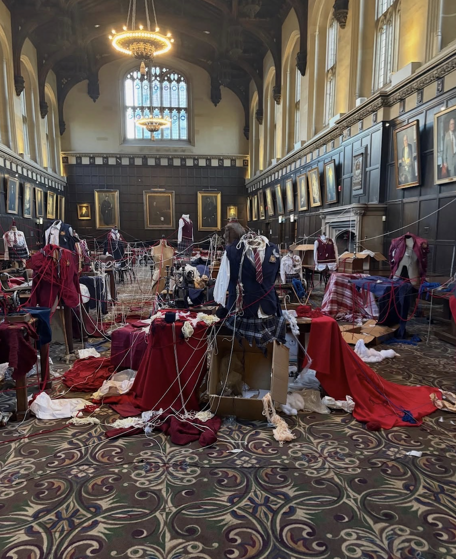 Kai Cenat’s Streamer University art direction by Nausha Turner, featuring a historic university hall transformed with burgundy uniforms, mannequins, layered fabrics, props, and interconnected threads for an immersive installation.