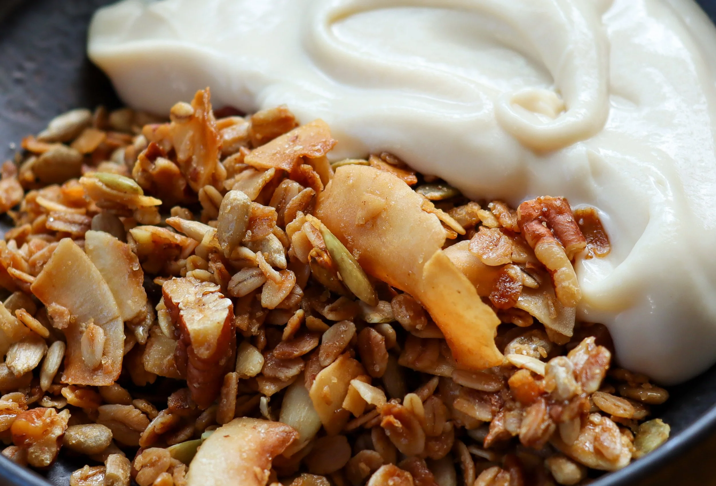 Close-up of granola with oats, nuts, and seeds next to a dollop of creamy yogurt.