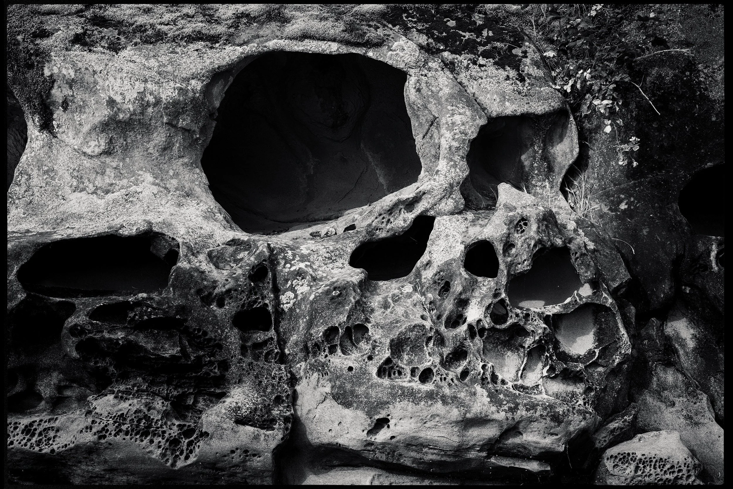 A black and white photograph of a human skull made out of rocks, with detailed textures and multiple holes and cavities.