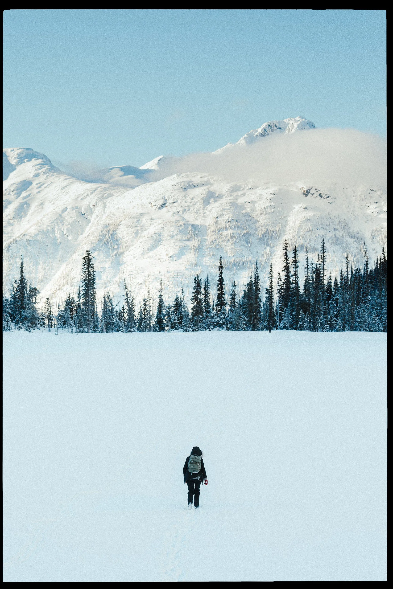 Person walking through a snow-covered landscape towards distant mountains.