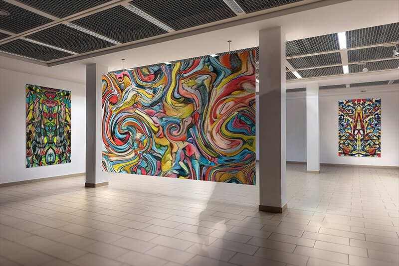 Three paintings hanging on a lightly colored art gallery wall. One in the foreground, another slightly behind it, and one in the background. The artwork featured is "Prelude", "Growth" and "Chief."