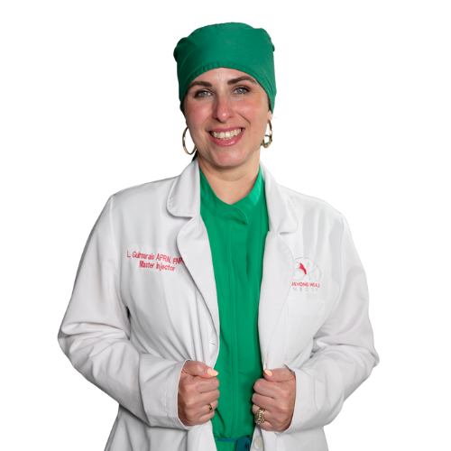 A female medical professional in scrubs and a green head covering, smiling, wearing a white lab coat with embroidered text.