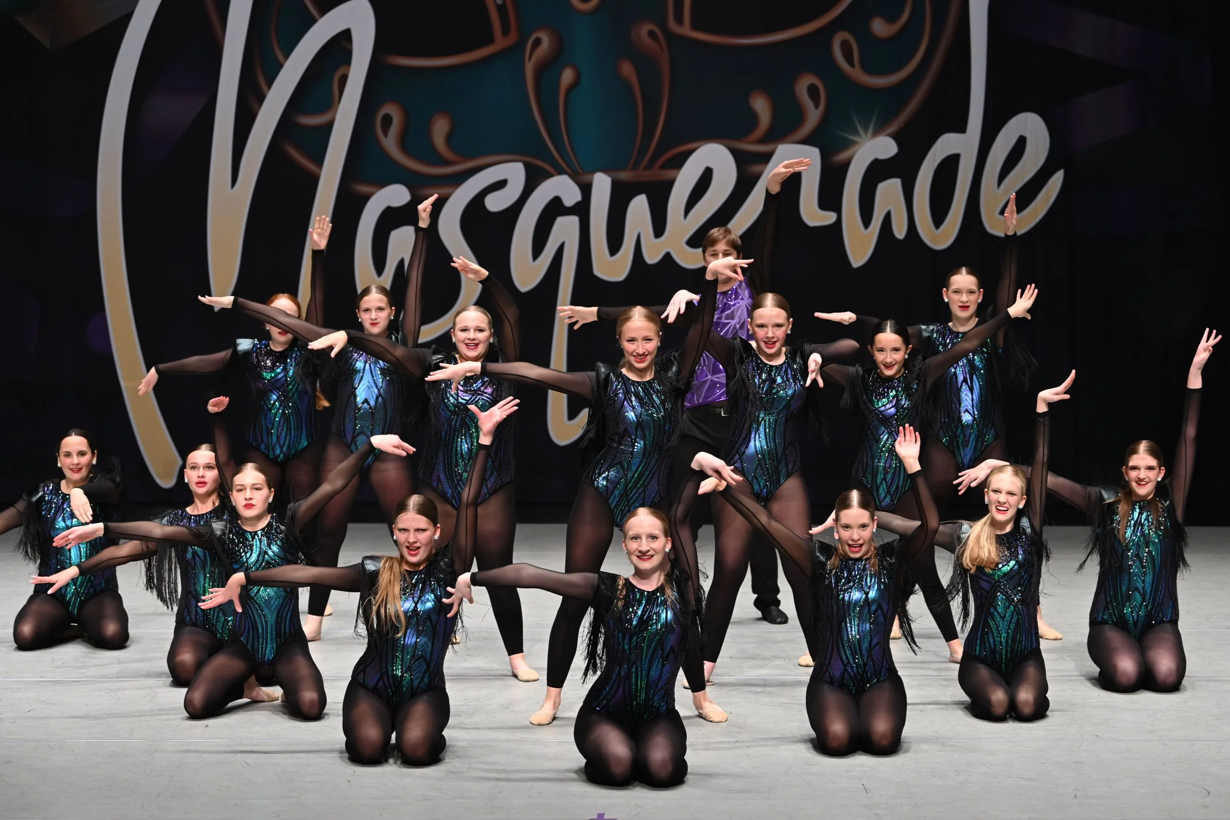 Group of young dancers in colorful costumes performing on stage at a dance competition.