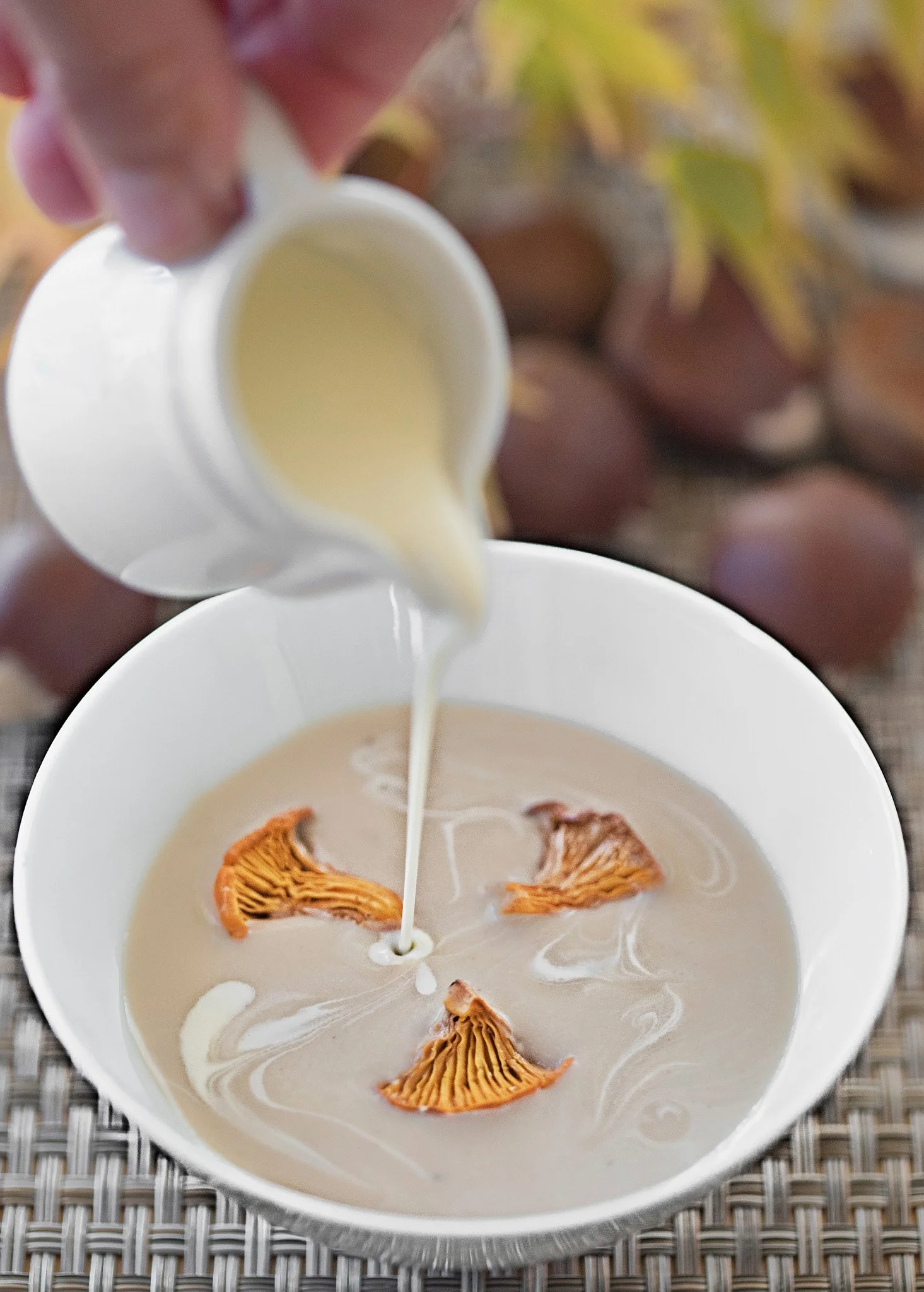 Pouring cream into a bowl with orange mushrooms submerged in a creamy liquid, with grapes and fall leaves in the background.