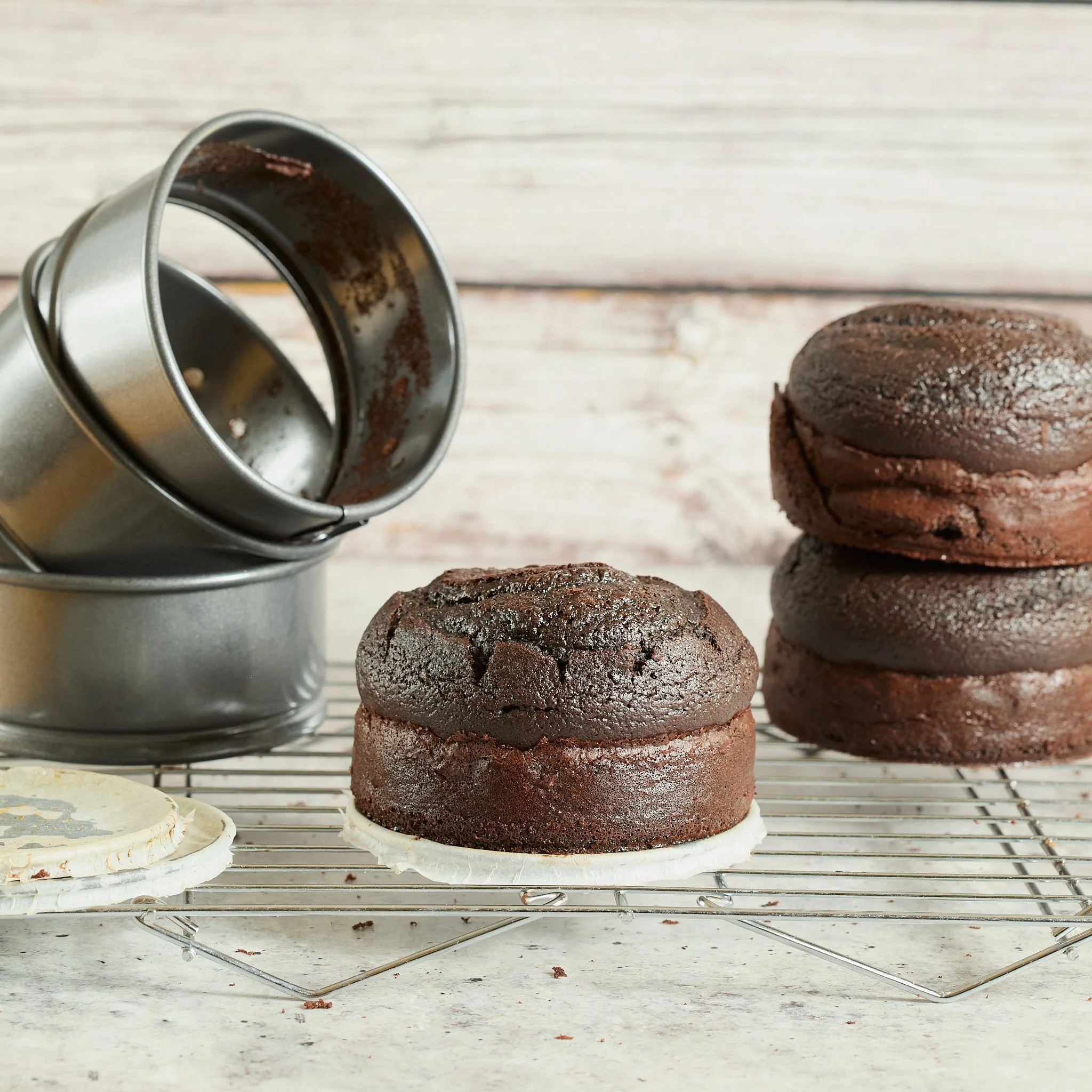 Stacked and individual chocolate muffins on a cooling rack with baking tins in the background