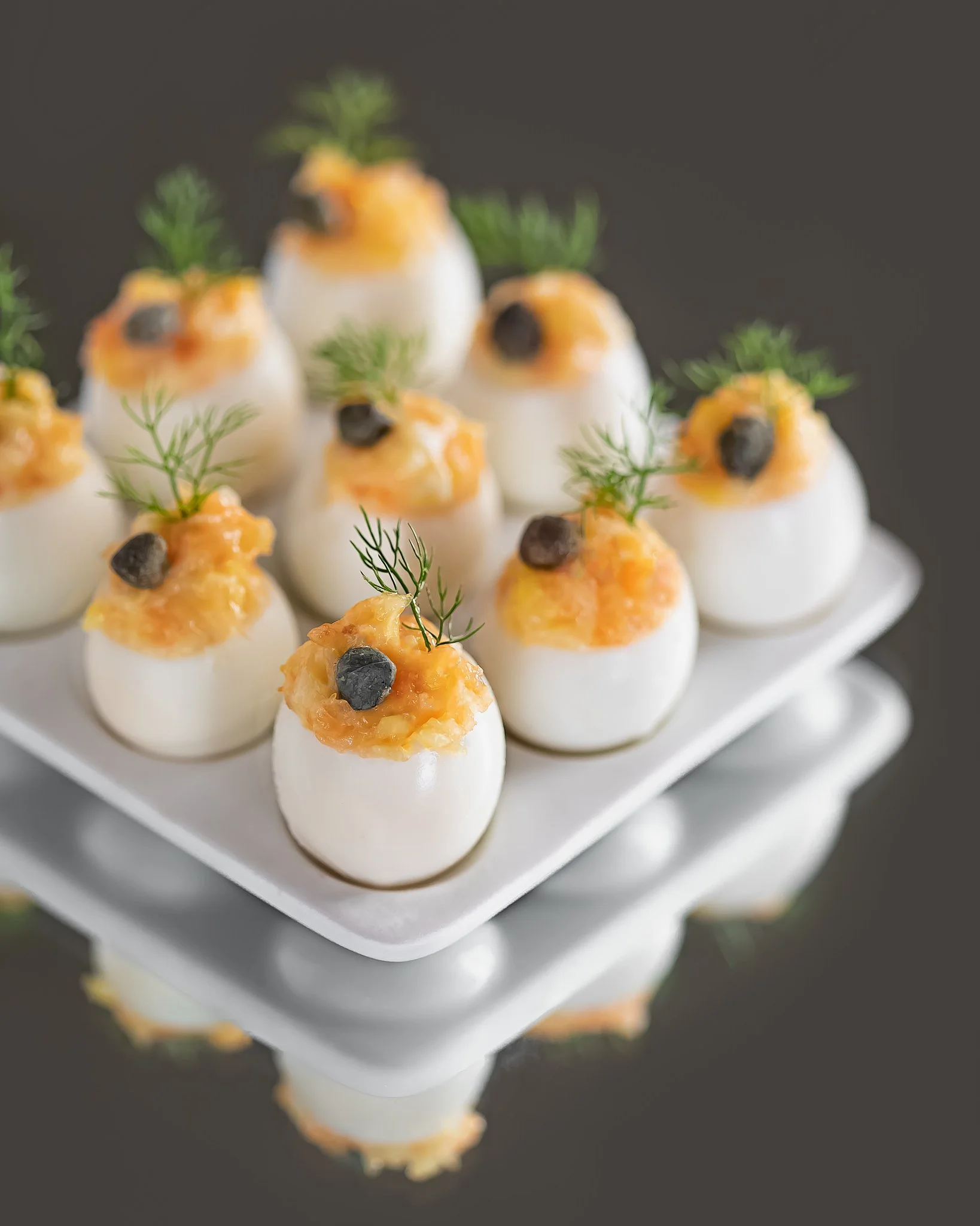 Deviled eggs topped with mustard, dill, and black pepper on a white platter