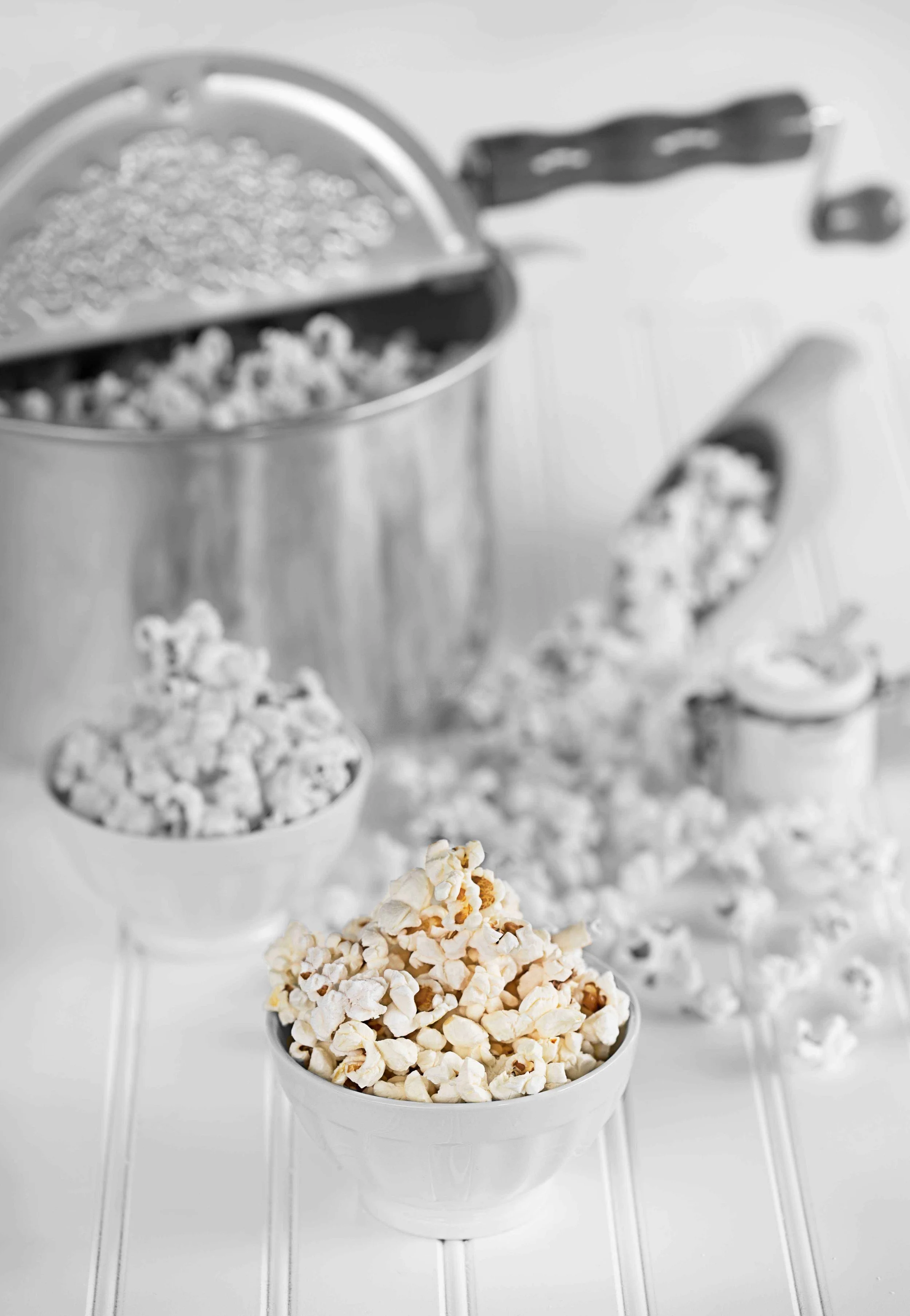 Bowl of popped popcorn with a metal container and scoop of additional popcorn in the background.