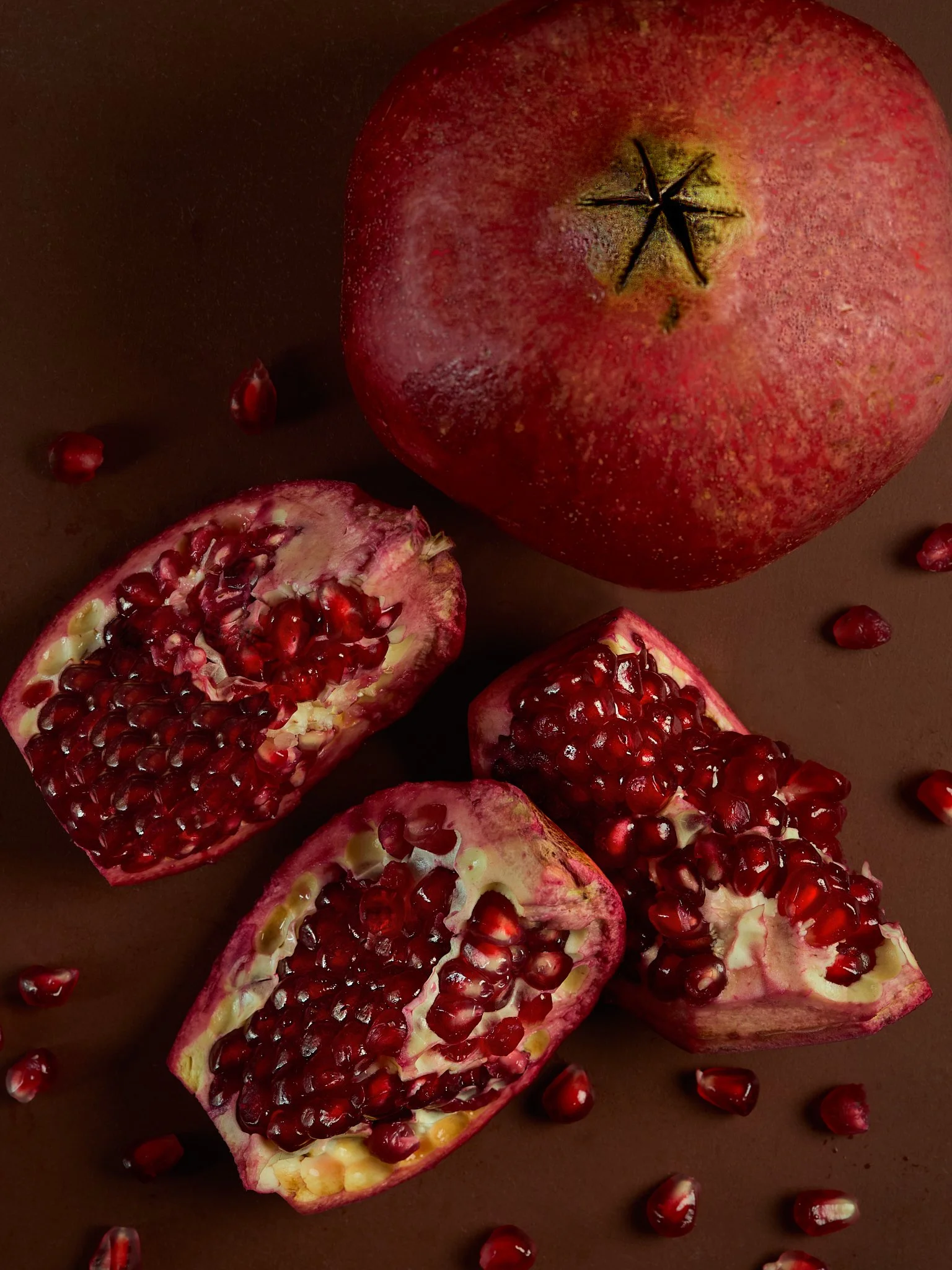 Whole pomegranate and three pomegranate halves with seeds on a brown background