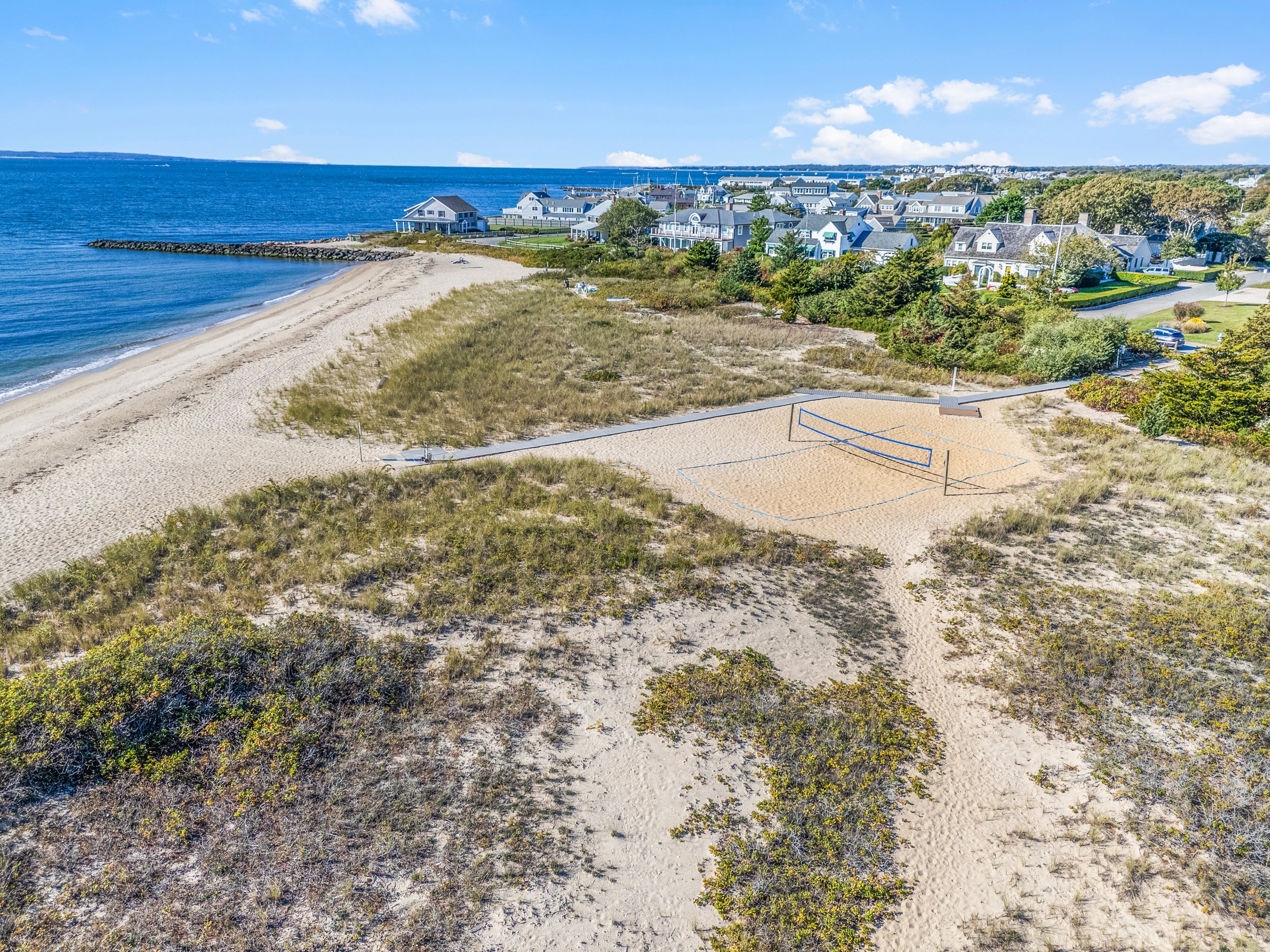 A beach with volleyball courts near a residential neighborhood, ocean in the background, and sunny skies.