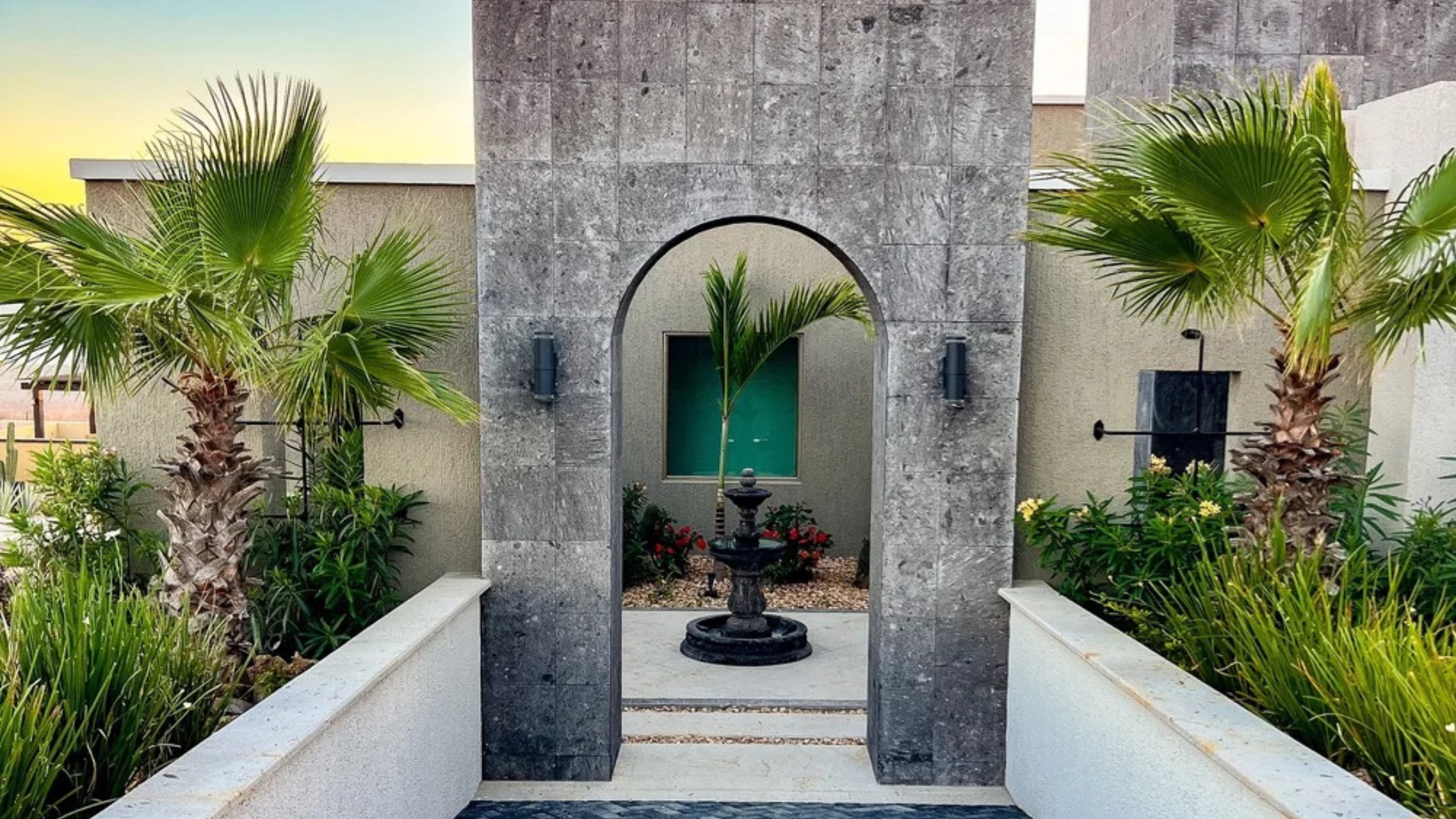 Luxury Cabo home construction showcasing modern stone pillars and clean architectural lines against a sunset sky.