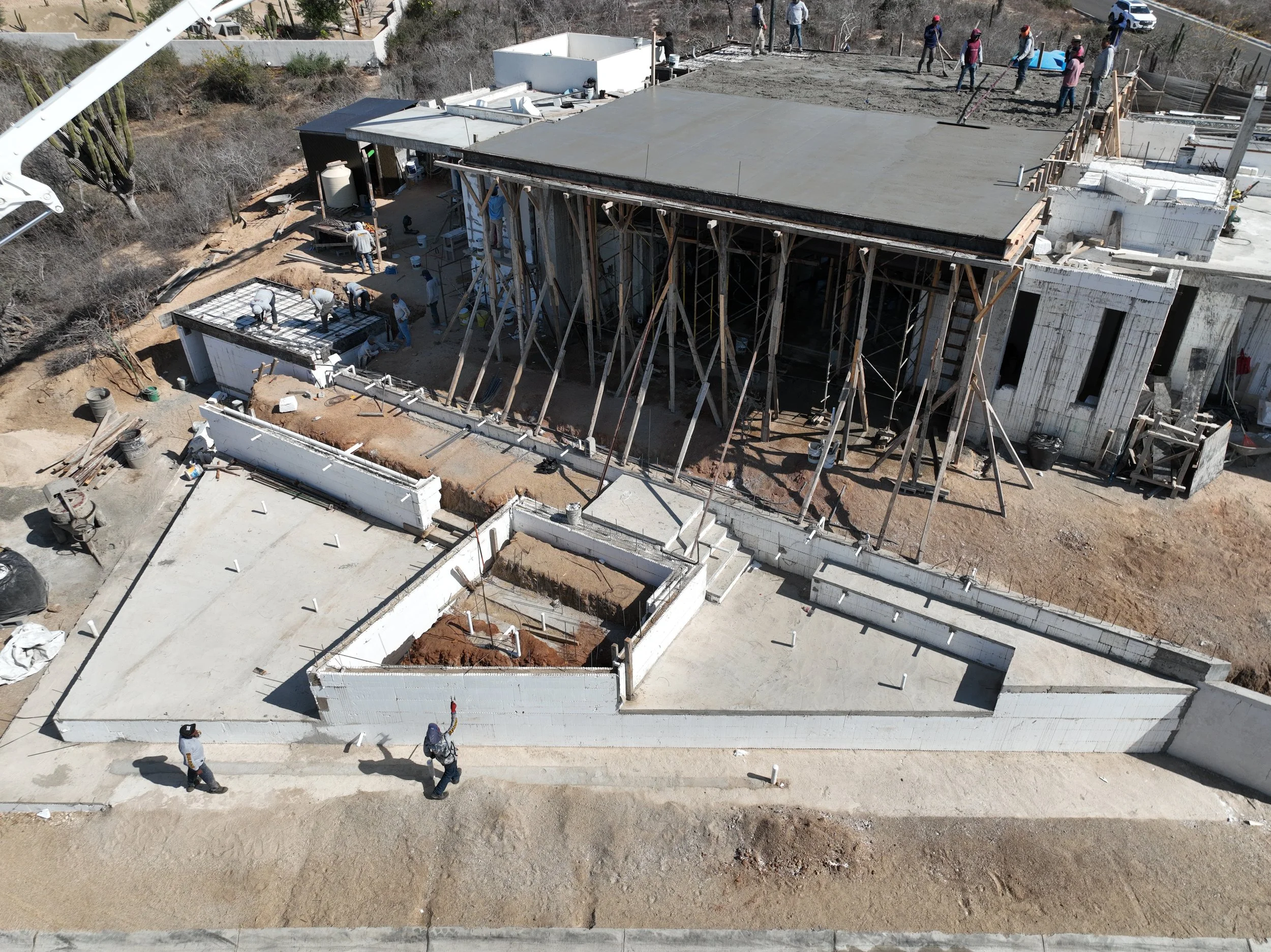 High-angle view of a construction crew pouring Insulated Concrete Form, with the structure supported by extensive wooden scaffolding.