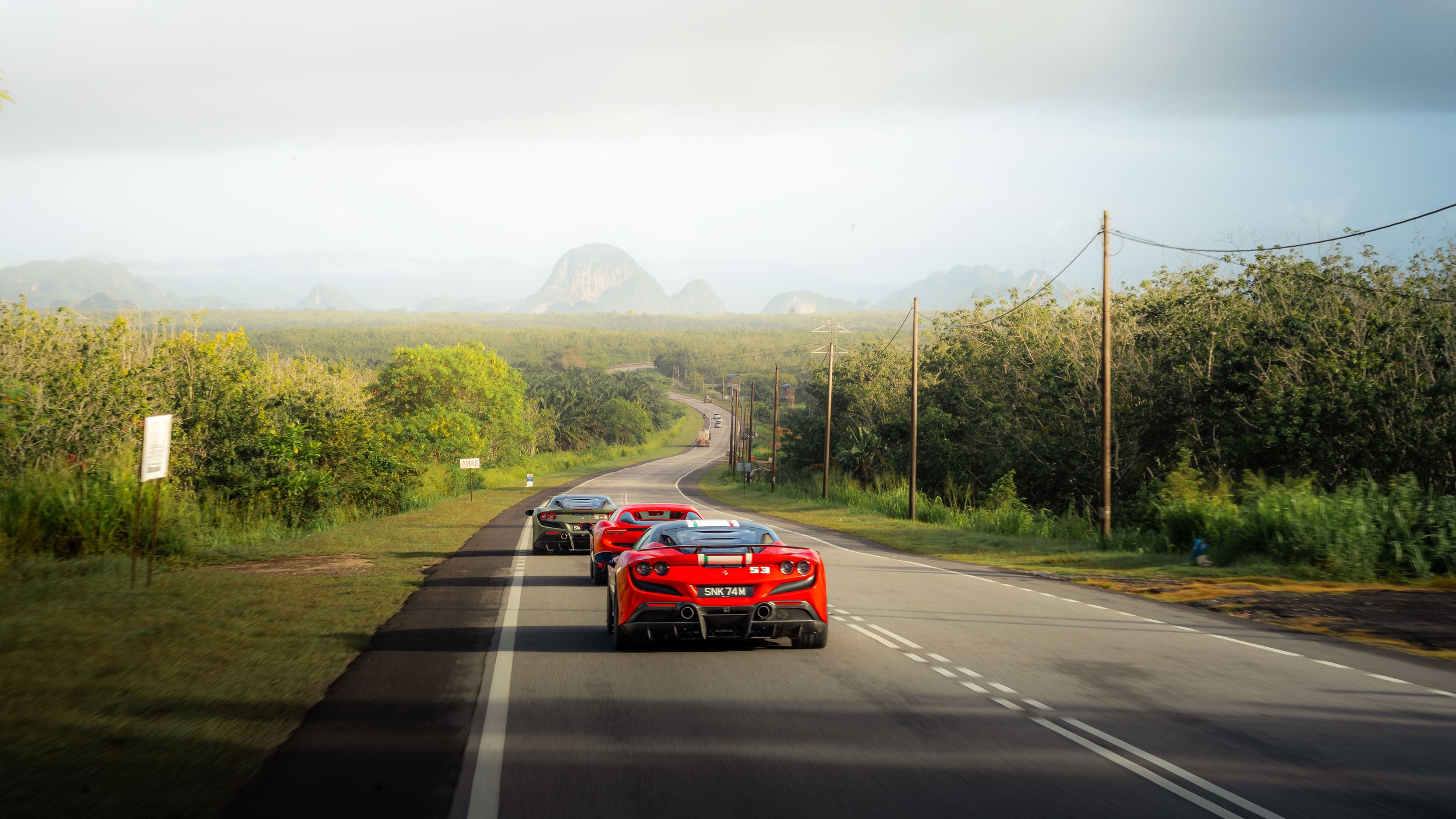 Rear view of a Ferrari convoy driving towards Krabi's limestone mountain landscape during the Ferrari Owners' Club Singapore Overseas Drive in Thailand.