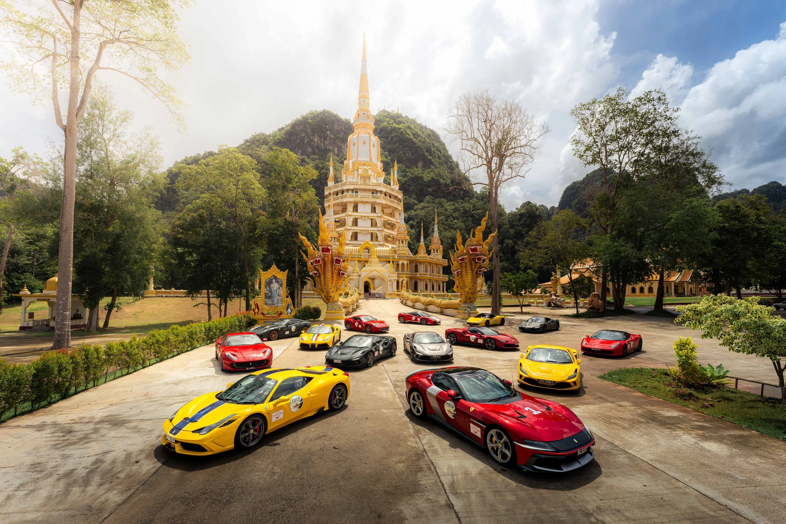 Ferrari Owners Club Singapore convoy parked in front of Wat Tham Suea (Tiger Cave Temple) in Krabi, Thailand, during the Ferrari Owners Club Drives 2026. A collection of Ferrari sports cars surrounds the golden temple against a backdrop of lush limes