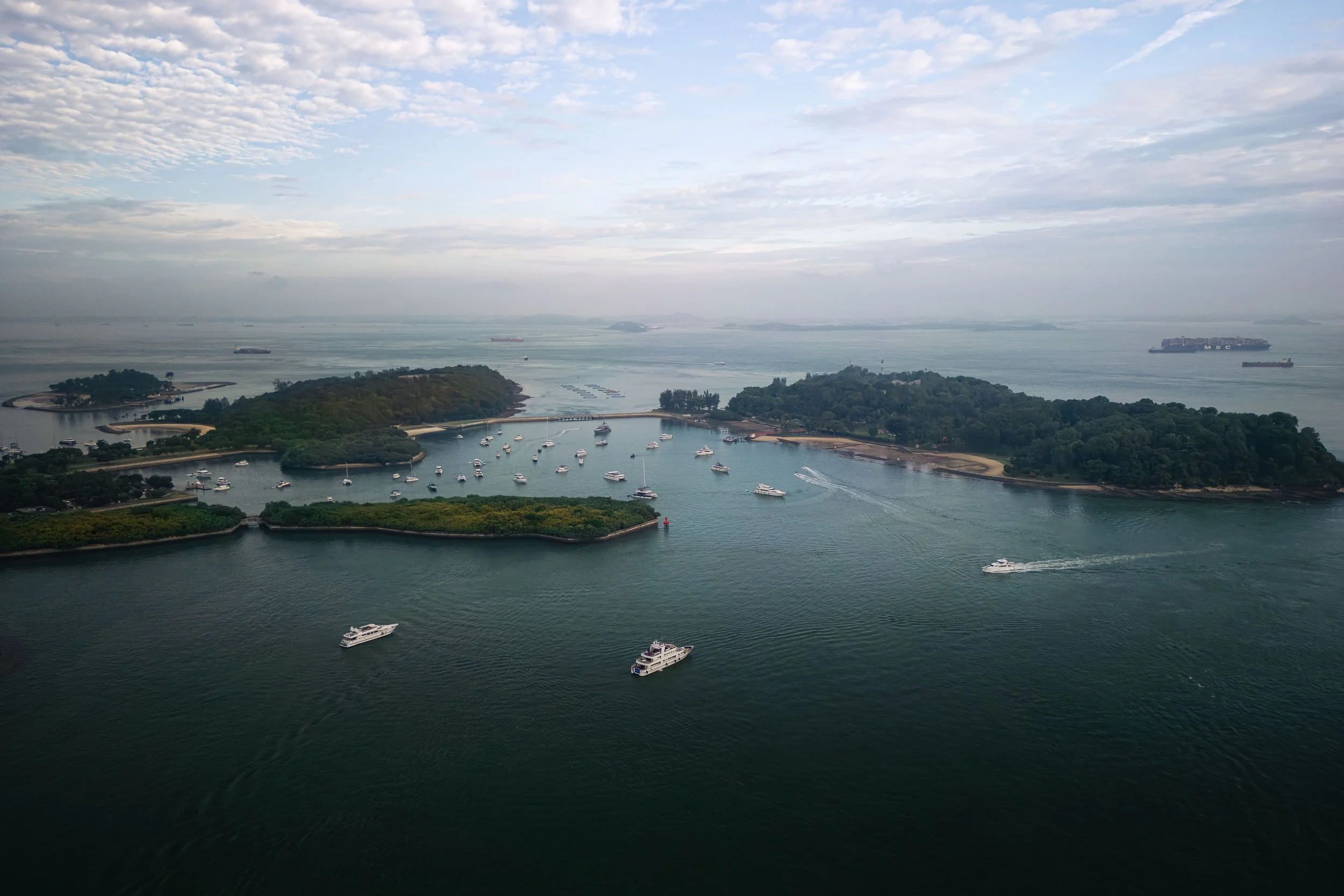 Aerial view of luxury yachts anchored off Singapore's Southern Islands, showcasing the scenic coastline, calm waters and premium setting for yacht events and waterfront experiences.