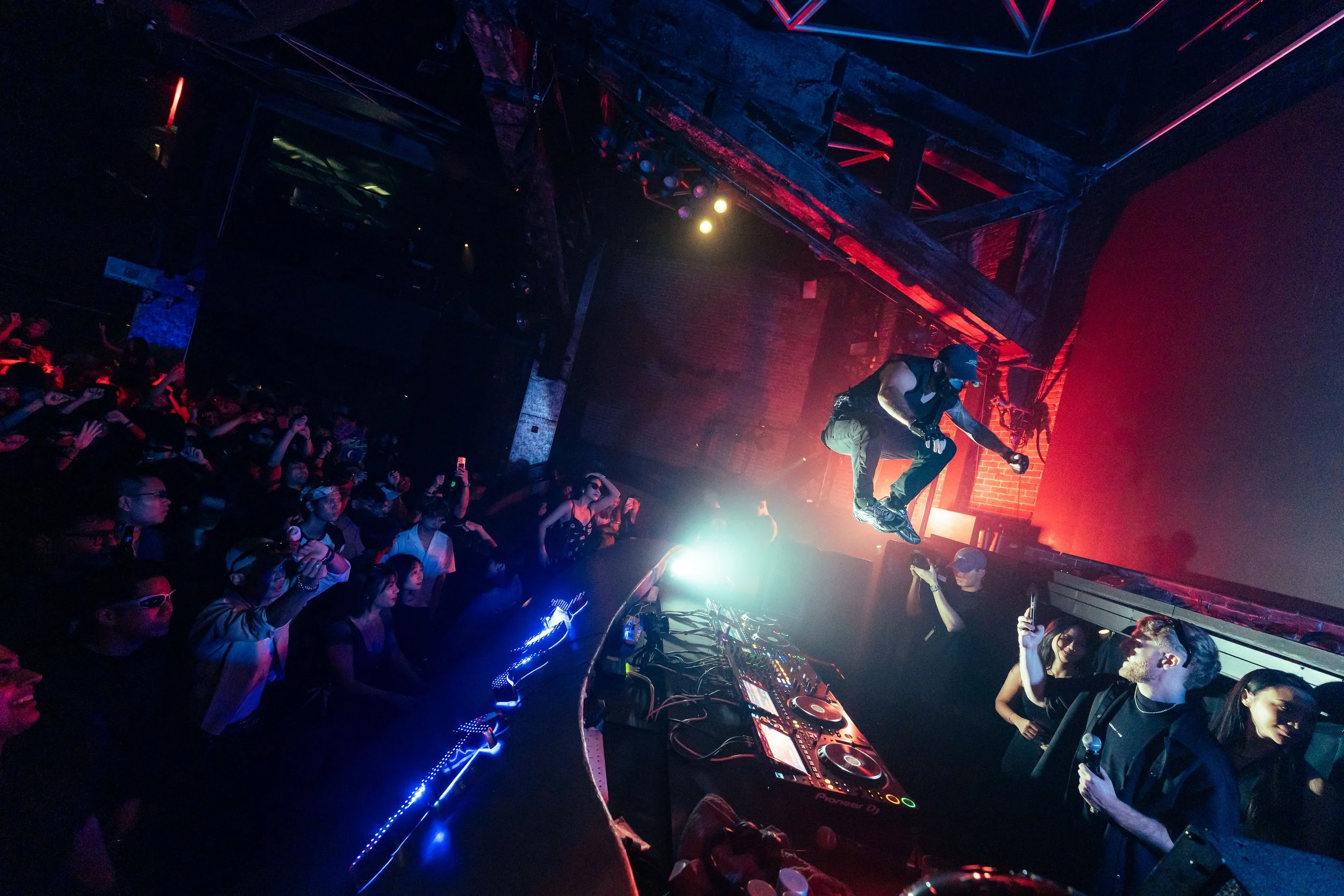 DJ MOJI performing live at Zouk Singapore, jumping above the DJ booth as a packed crowd cheers beneath dramatic stage lighting during a high-energy nightclub performance.