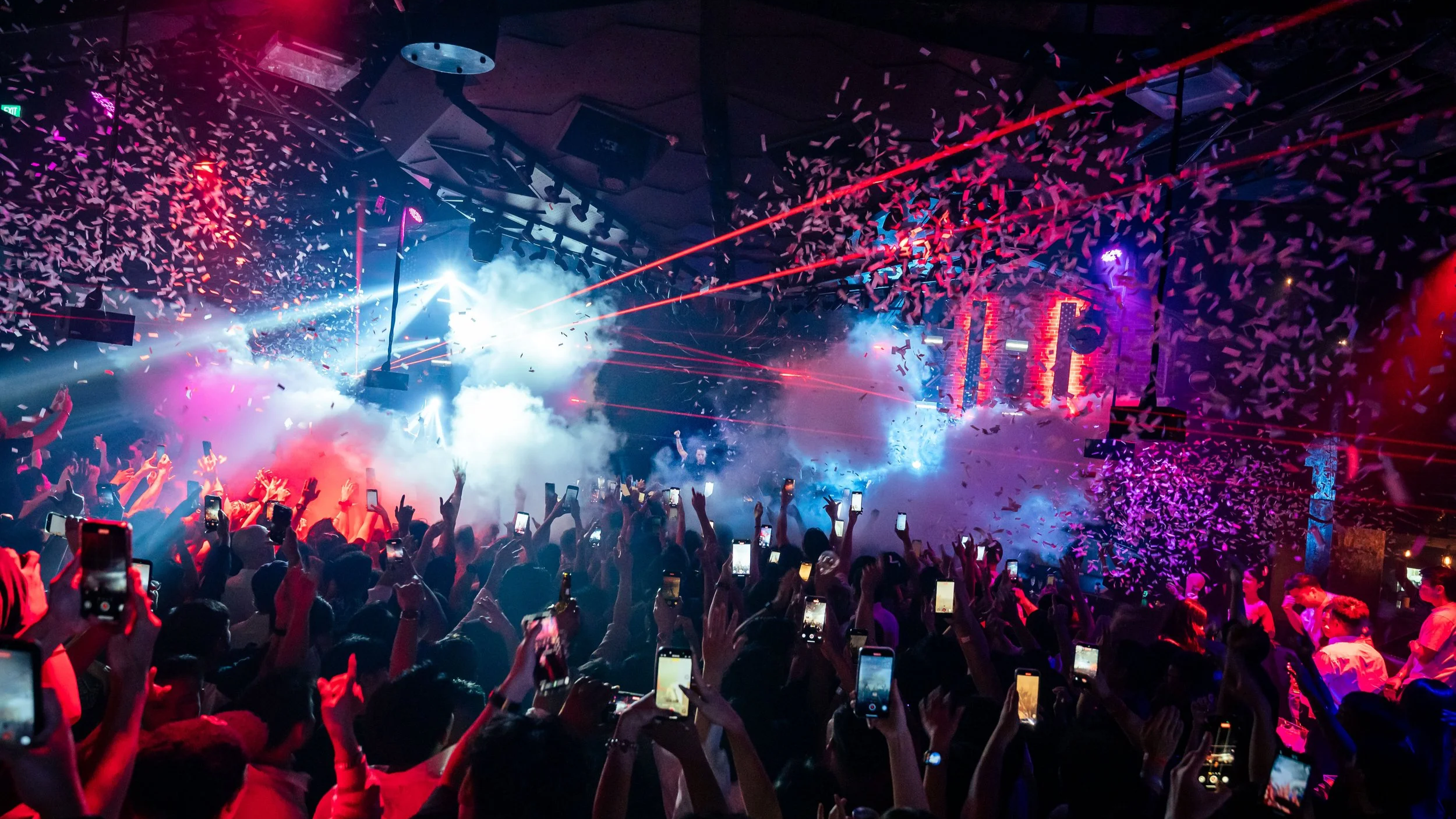 DJ Nicky Romero performing live at Zouk Singapore as confetti, CO2 effects and red laser beams fill the venue above a packed crowd during a high-energy electronic dance music performance.

