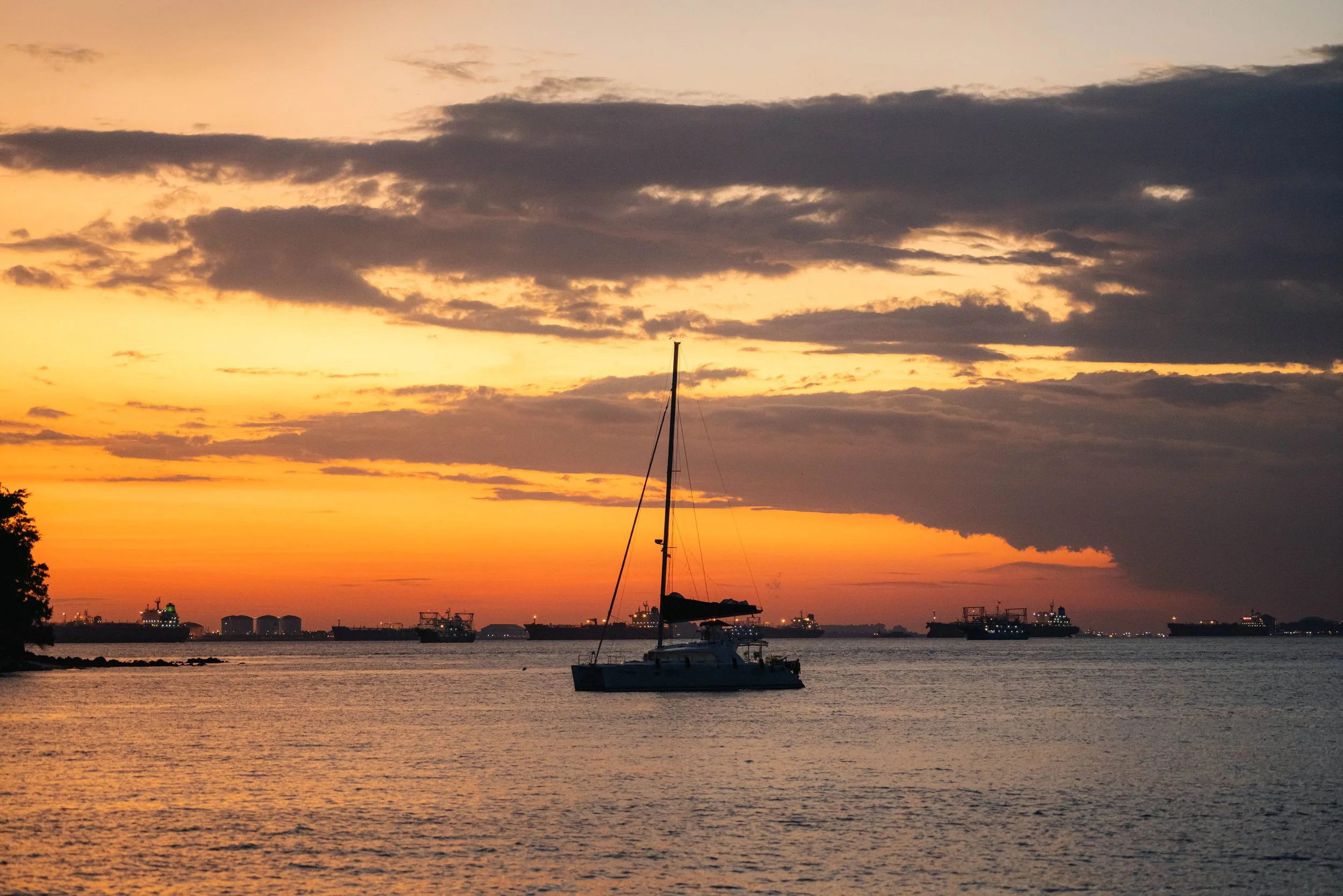 Luxury sailing yacht anchored off Singapore's Southern Islands at sunset, capturing a peaceful waterfront scene with golden skies, calm waters and a premium yacht lifestyle atmosphere.
