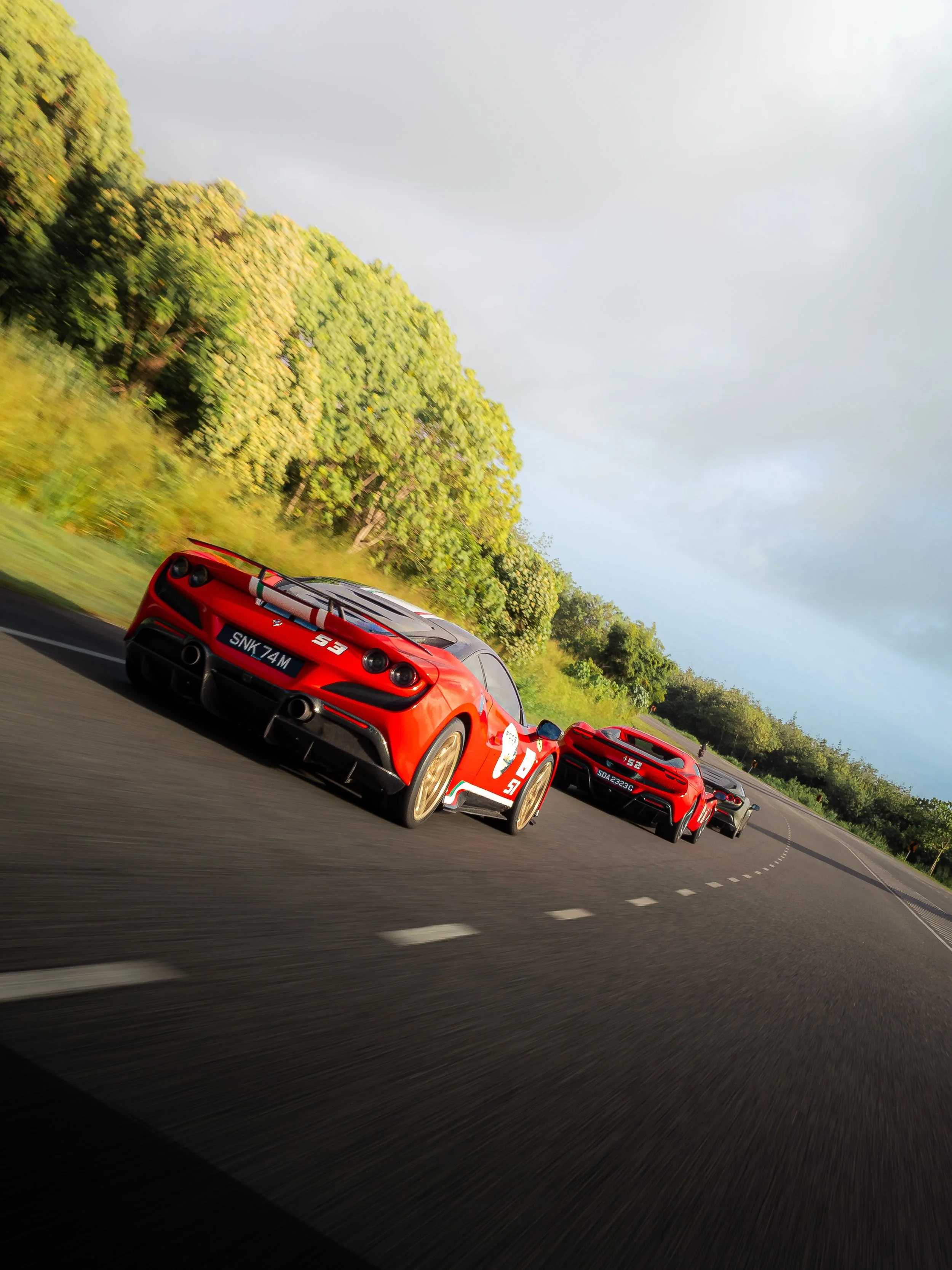 Rear view of Ferraris navigating a sweeping bend in Krabi, Thailand during the Ferrari Owners' Club Singapore Overseas Drive, showcasing a luxury supercar convoy.