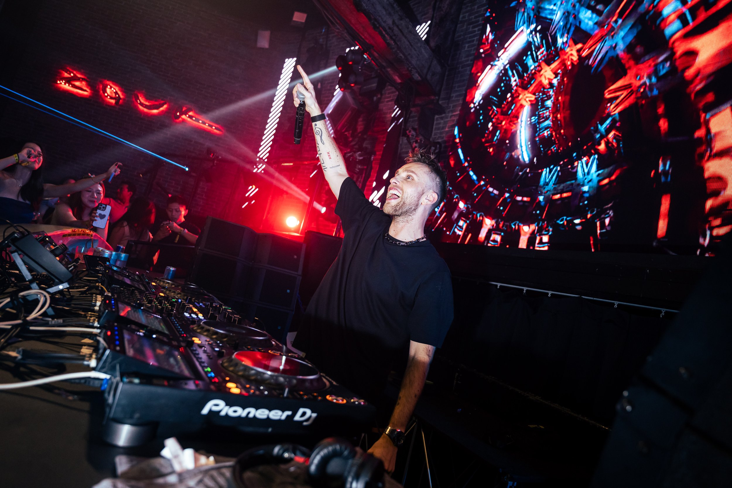 DJ Nicky Romero performing live at Zouk Singapore, raising his hand above the DJ booth as immersive LED visuals and vibrant stage lighting energise the crowd during a high-energy electronic dance music performance.