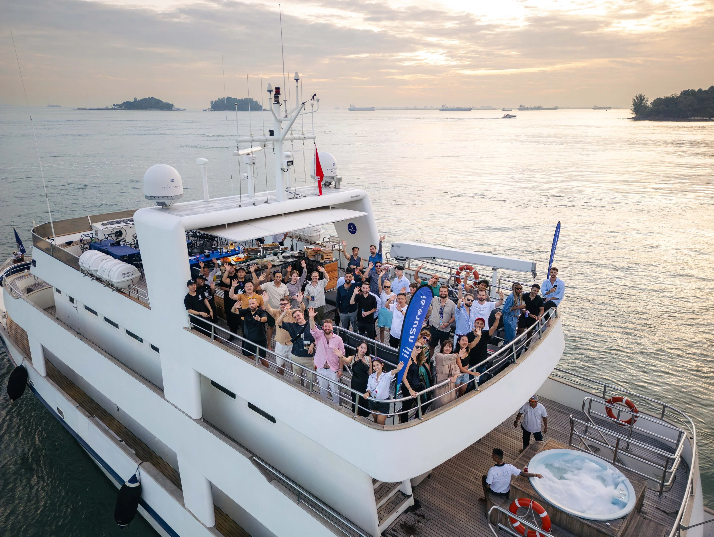 Aerial group photo aboard a luxury yacht in Singapore's Southern Islands, capturing guests at a premium corporate networking event with scenic waterfront views at sunset.