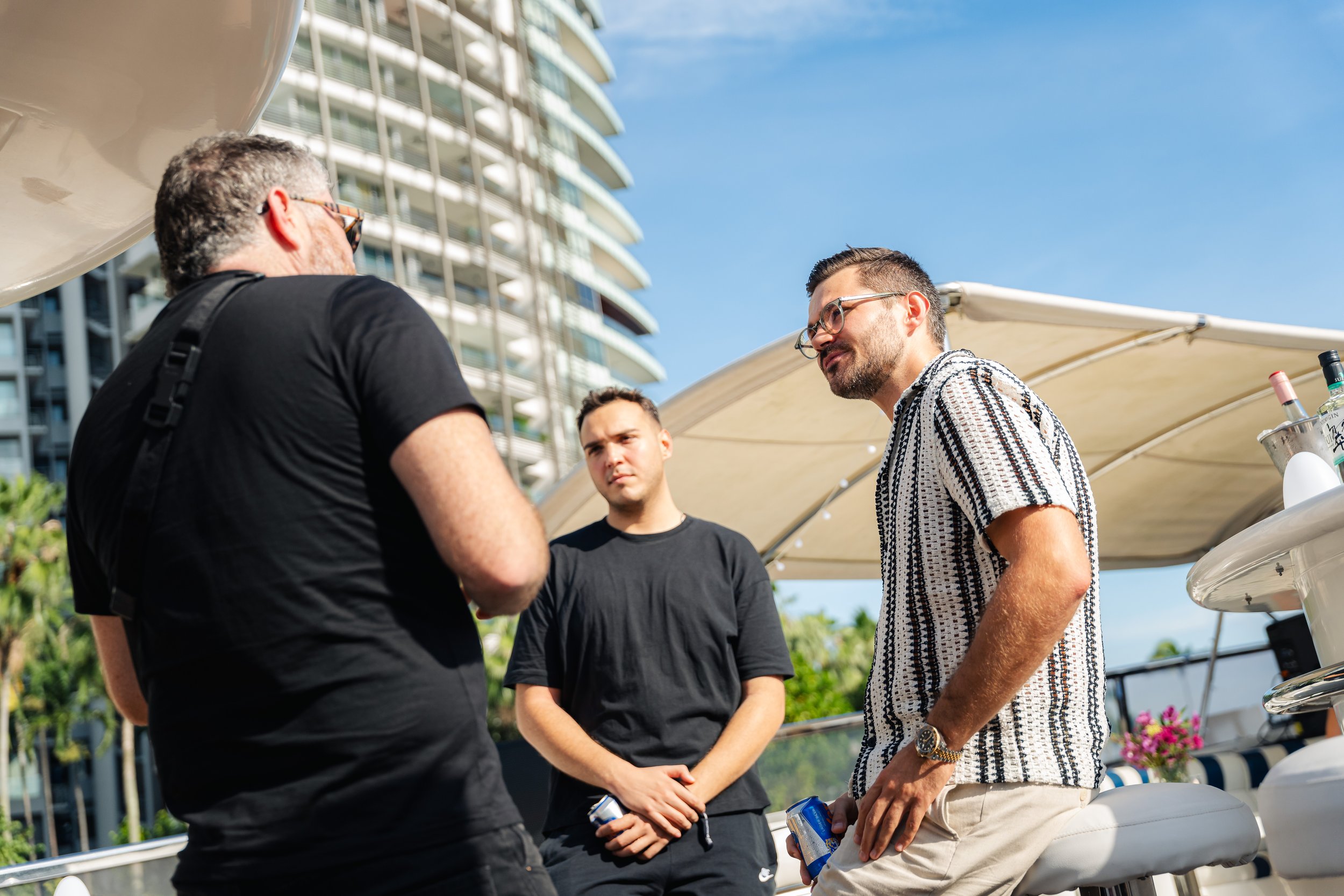 Guests networking aboard a luxury yacht during a cryptocurrency event, enjoying conversations in a waterfront setting with a modern marina skyline in the background.