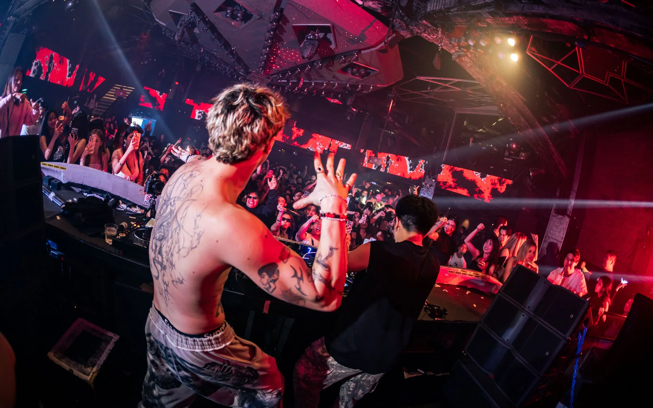 DJ Fantasm performing live at Zouk Singapore, engaging a packed crowd from the DJ booth as vibrant red stage lighting and immersive nightclub production create an electrifying electronic music atmosphere.