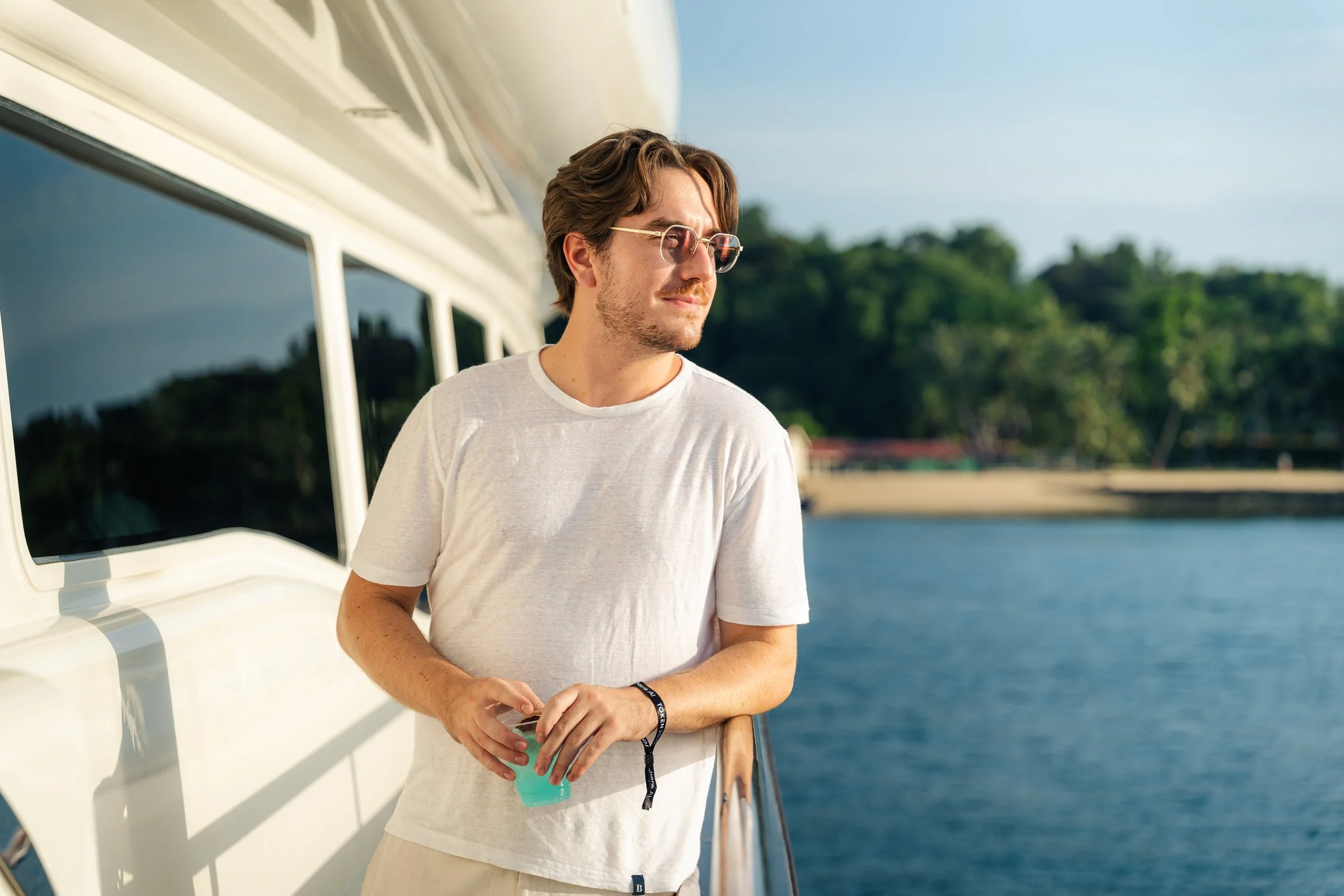 Guest enjoying the waterfront aboard a luxury yacht during a cryptocurrency networking event, captured in a relaxed lifestyle portrait with marina views in the background.