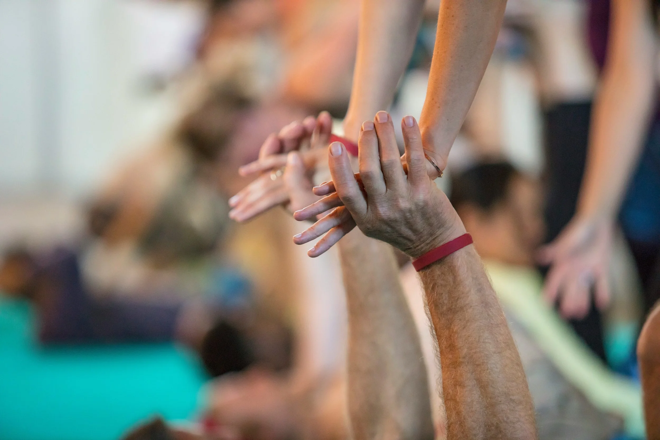 Close-up of hands stacked on top of each other during a group activity or exercise, with people blurred in the background.