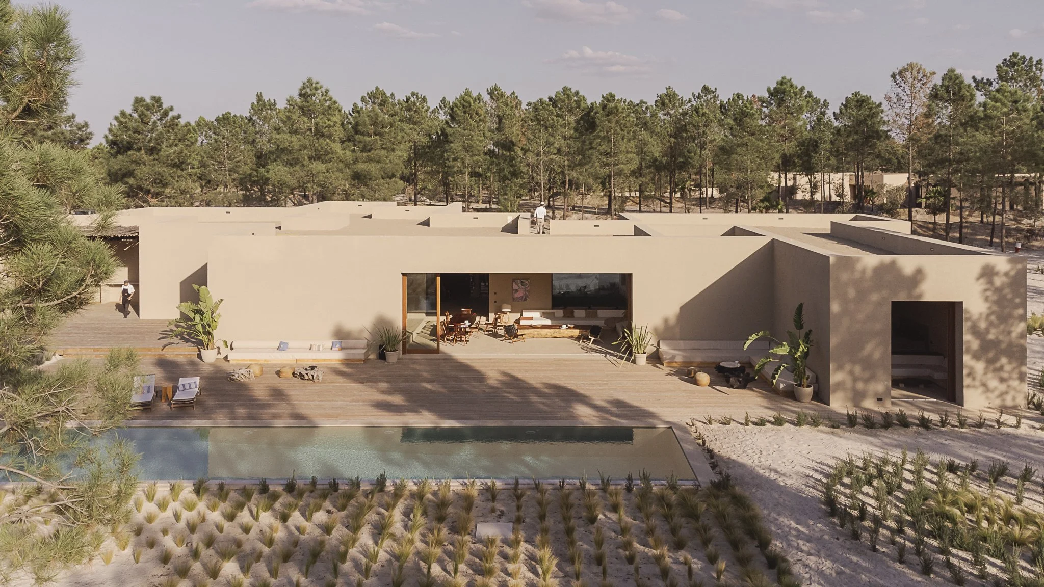 Modern house with outdoor pool, patio area, and surrounding desert landscape, trees, and sandy terrain.