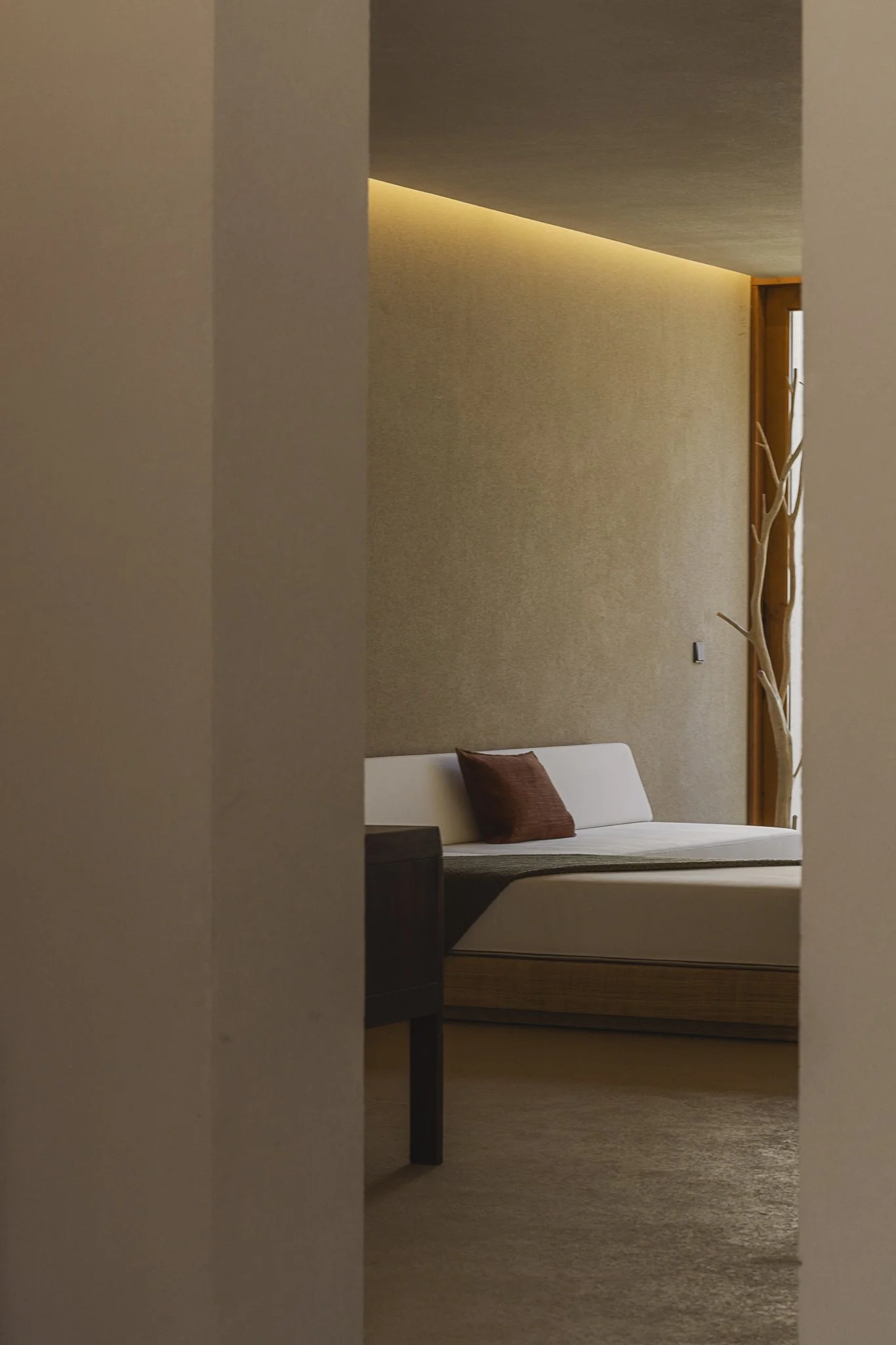 View of a hotel room with a white bed, brown cushion, beige walls, wooden details, and ambient lighting.