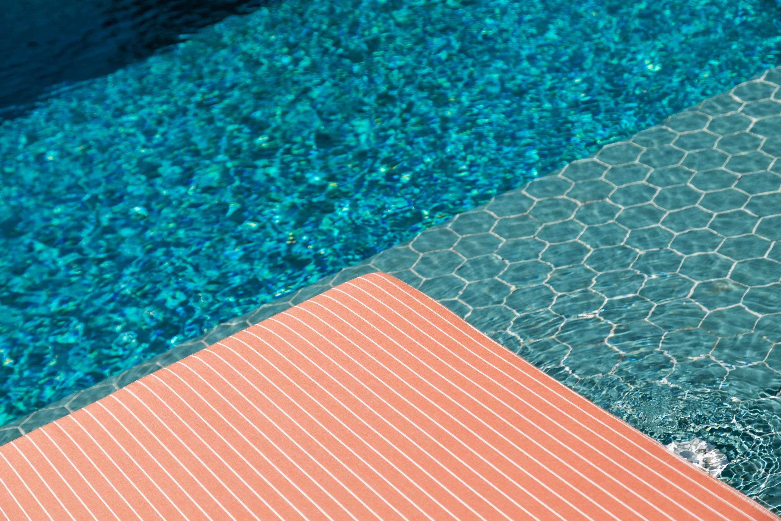 Close-up of a swimming pool with blue mosaic tiles, a hexagonal tile border, and a red striped pool deck.
