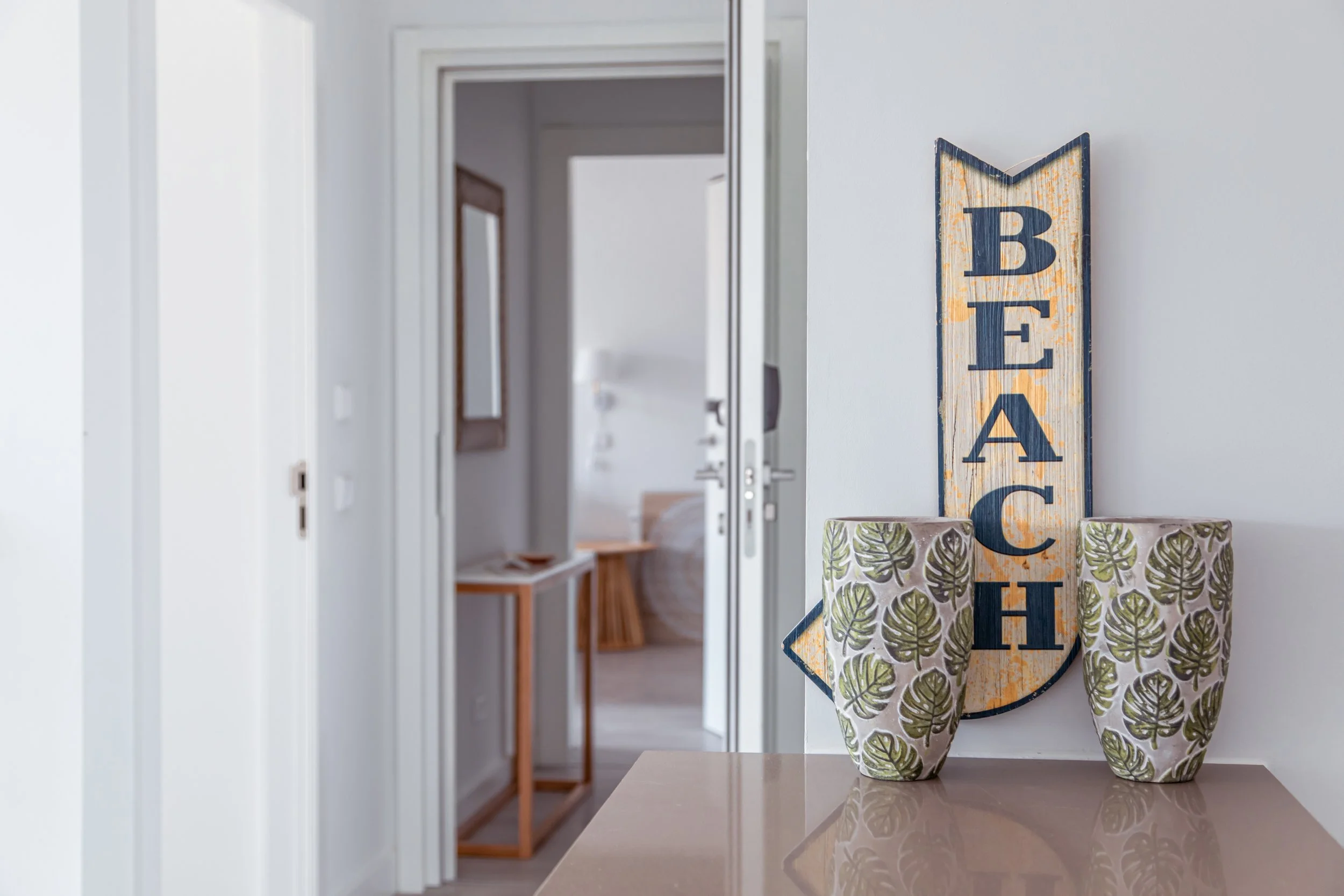 Decorative forget-me-not sign with floral vases on a table, placed inside a home near a hallway with visible bedroom in the background.