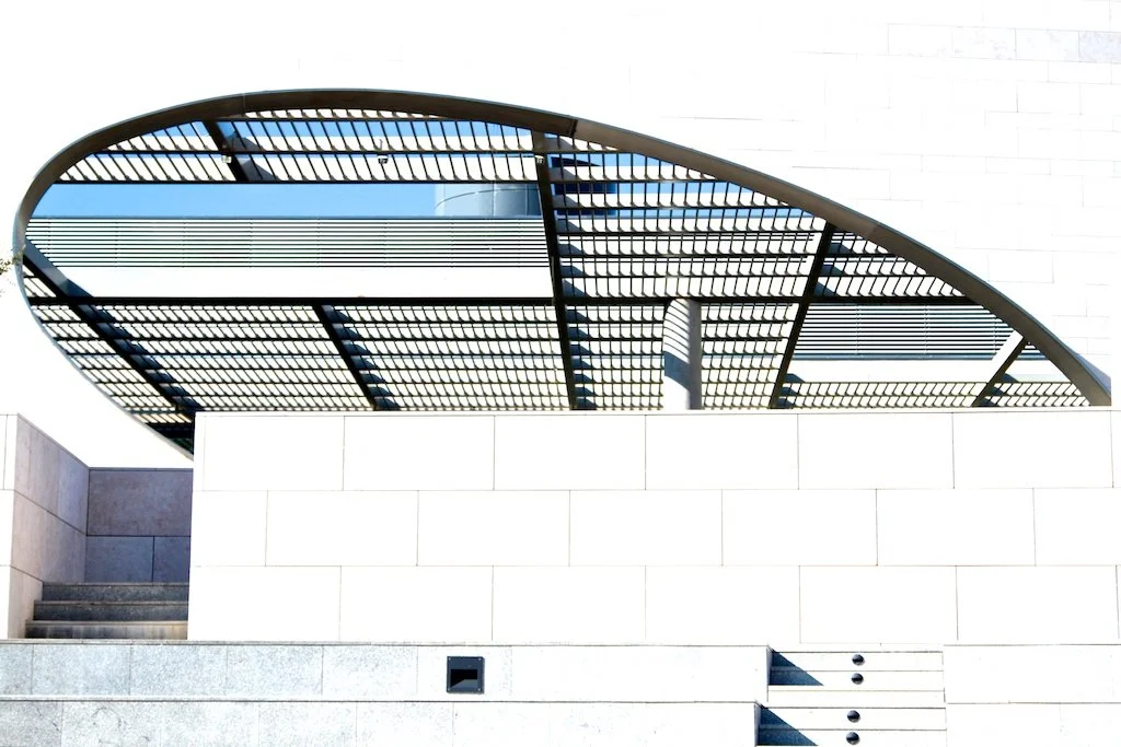 Modern architectural building with a curved metal and glass roof structure above a white stone wall.