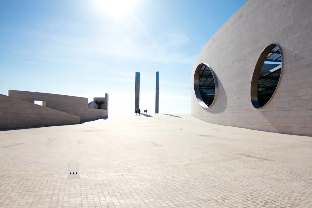 Modern architectural building with circular windows and a smooth curved exterior, under a bright blue sky.