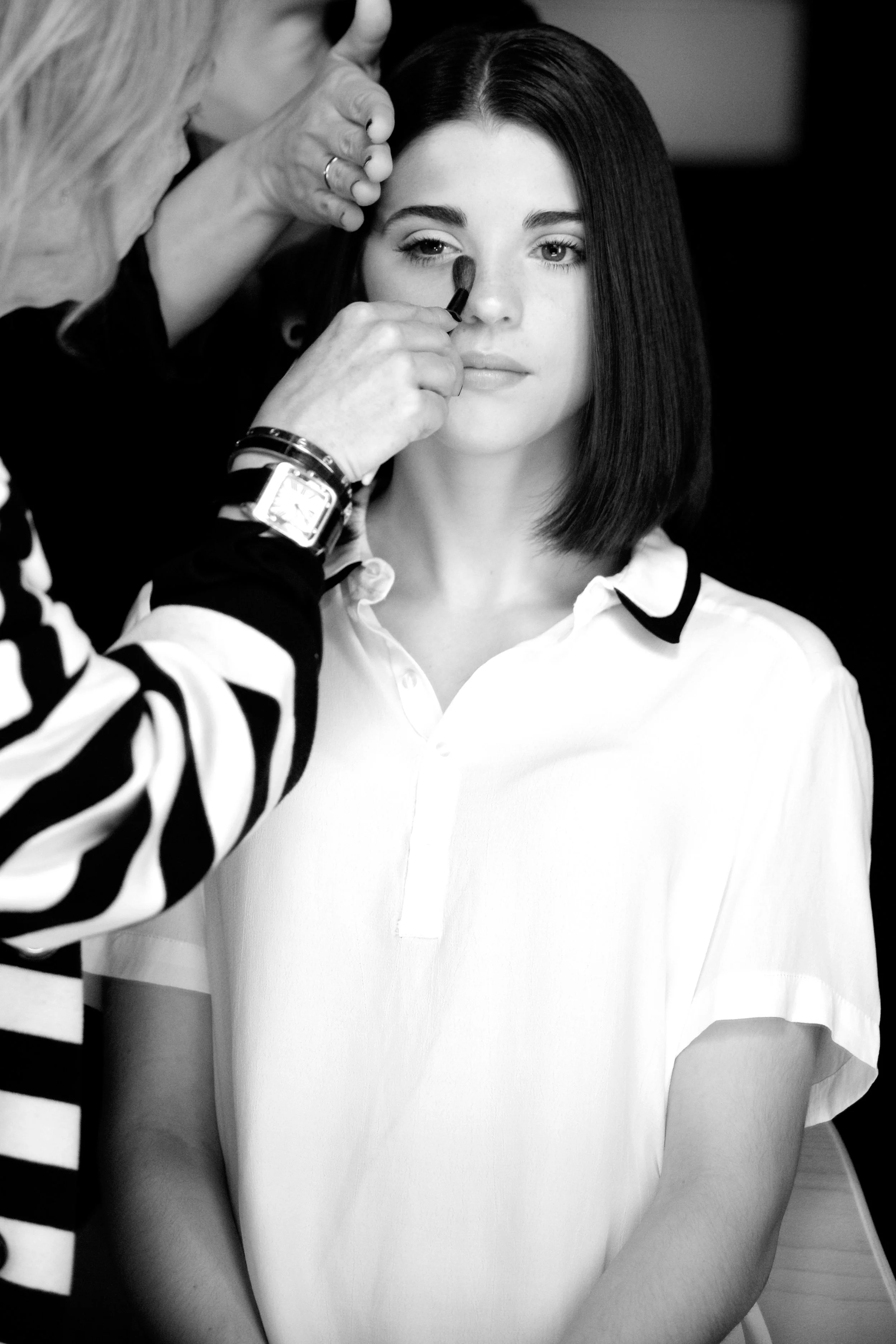 A woman with dark hair getting her makeup done by a makeup artist.