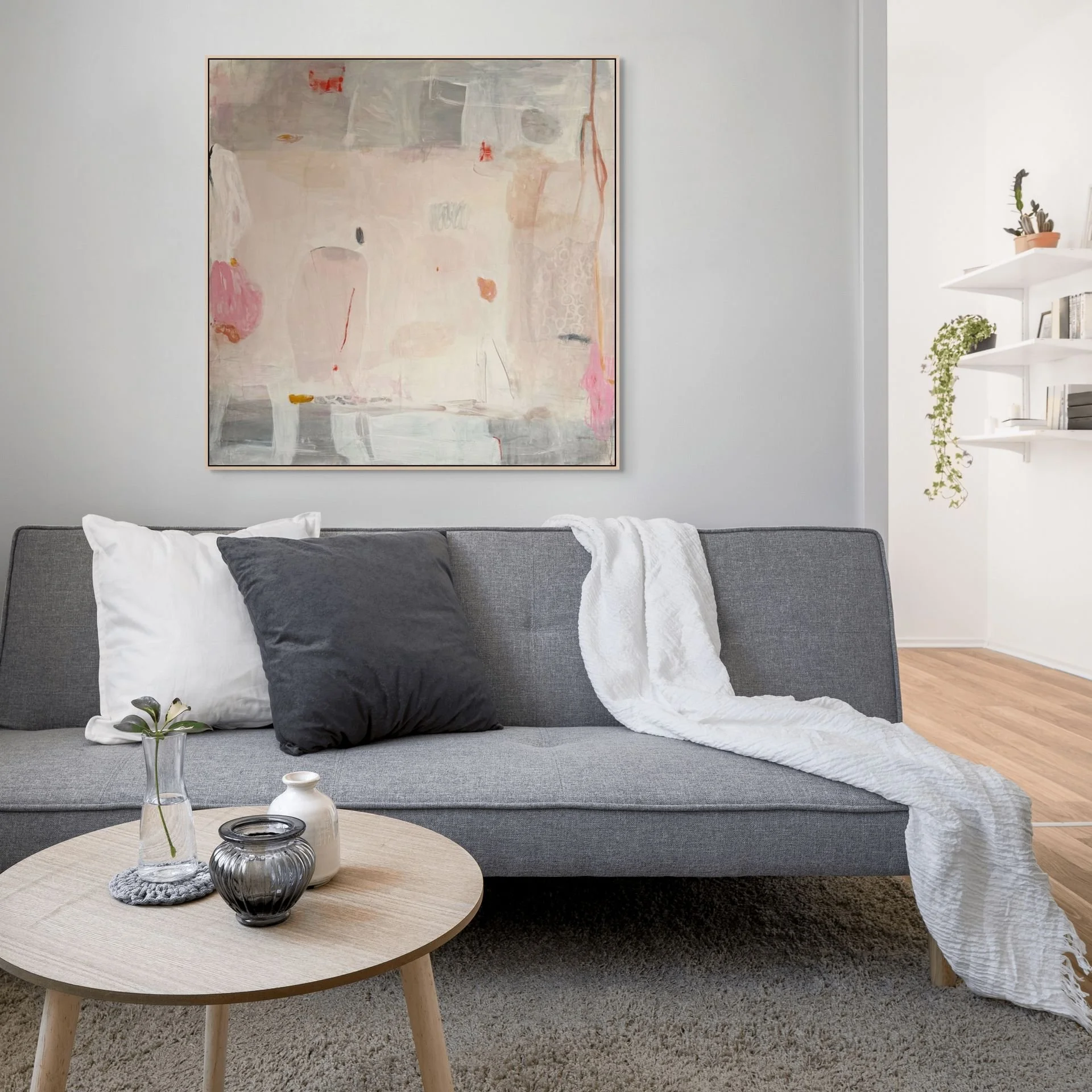 Pink, gray, and cream framed abstract art print by Laurie Baars shown in a living room with a gray sofa.