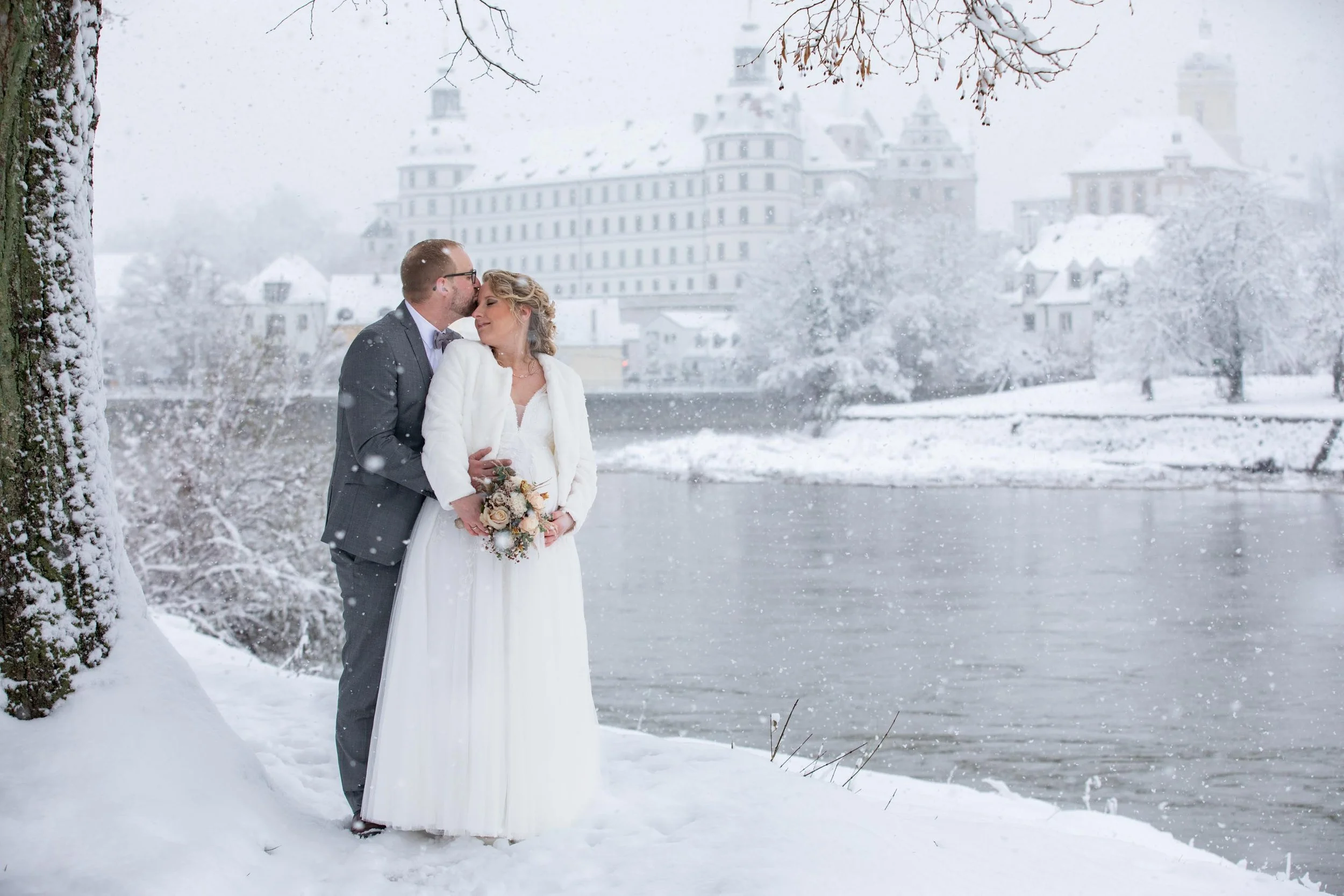Hochzeit im Winter. Das Foto ist vor verschneiter Kulisse des Neuburger Schlosses aufgenommen bei Schneefall