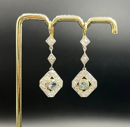 A pair of gold and diamond dangle earrings on a black background.