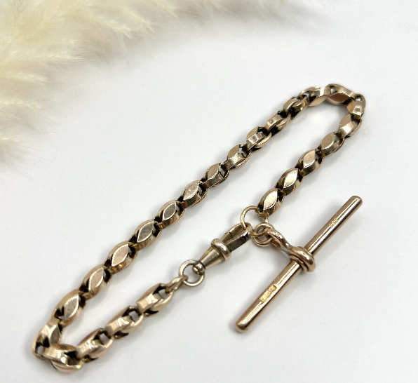 Gold bracelet with t-bar on a white surface