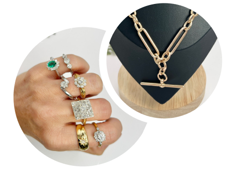 A hand wearing multiple gold with gemstones, next to a jewellery display featuring a gold Albert chain on a black stand.
