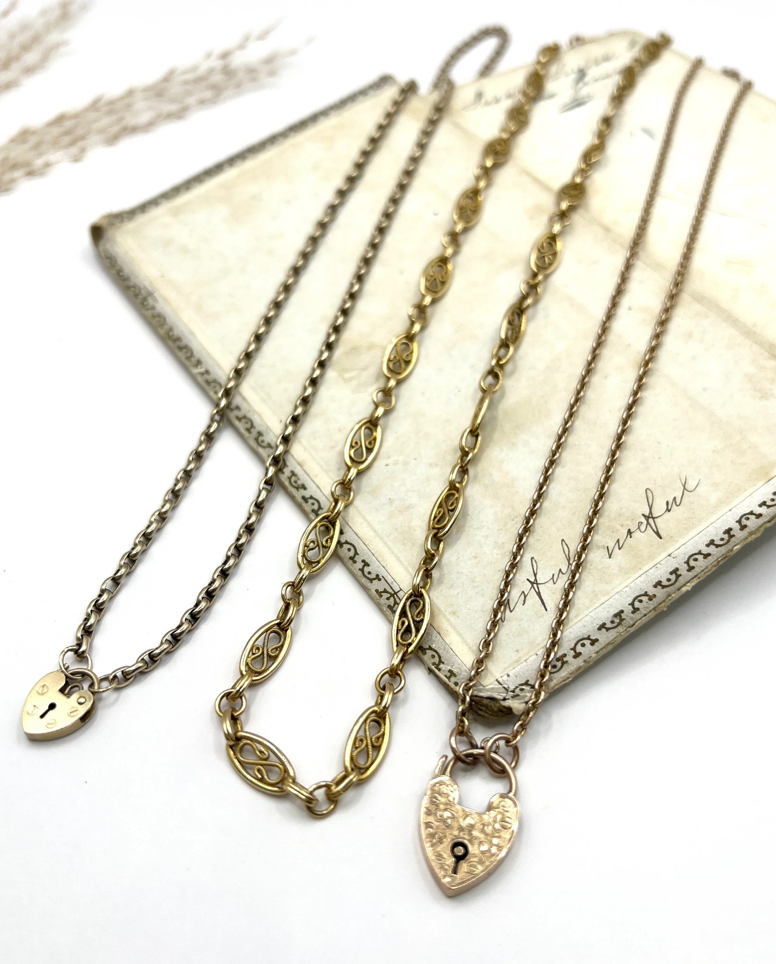 Collection of gold necklaces with heart-shaped lockets and decorative links, laid out on an antique book background.