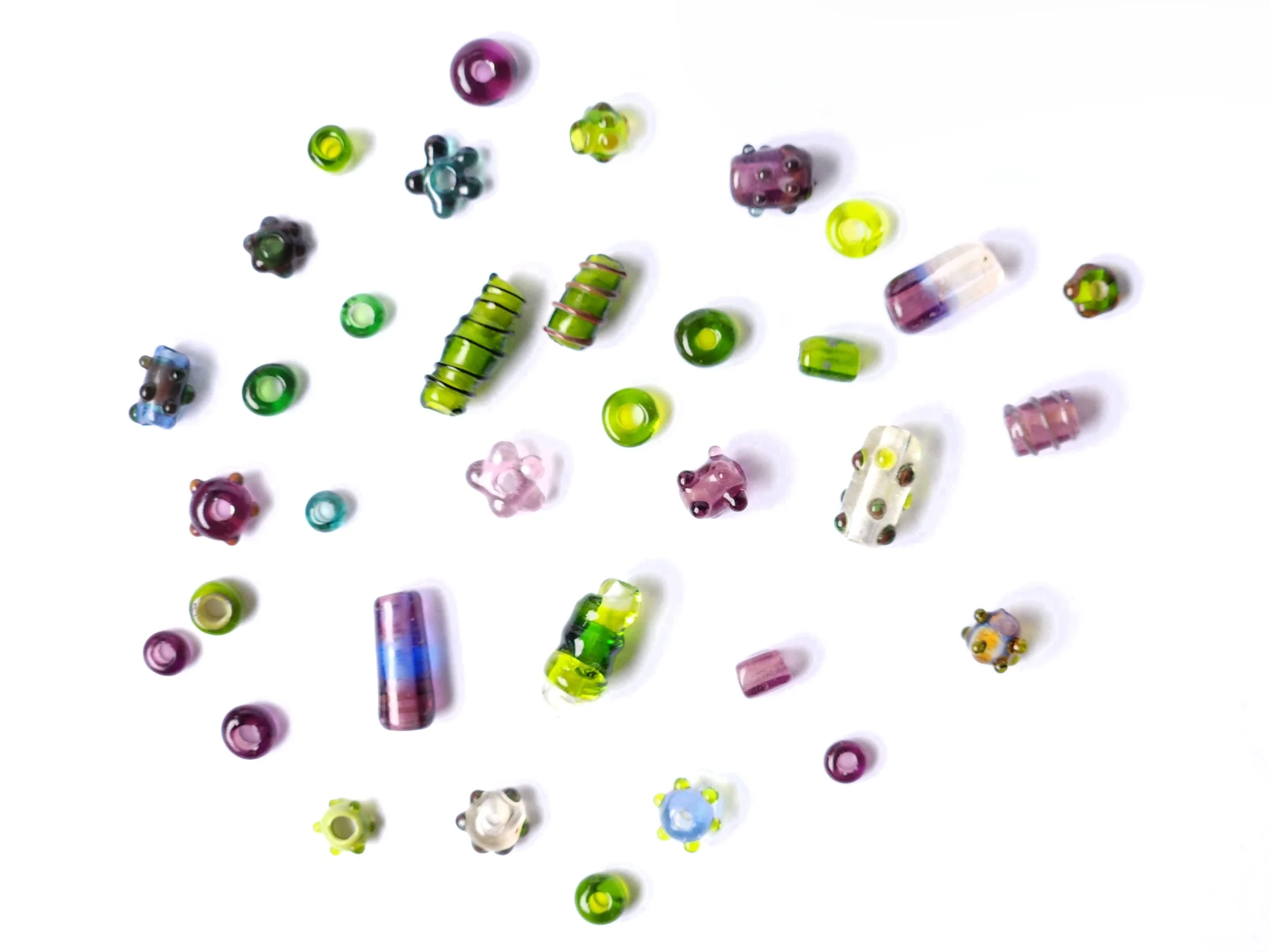 Lampworked beads in blue and green glass hues. Variety of handmade glass beads spread out. 