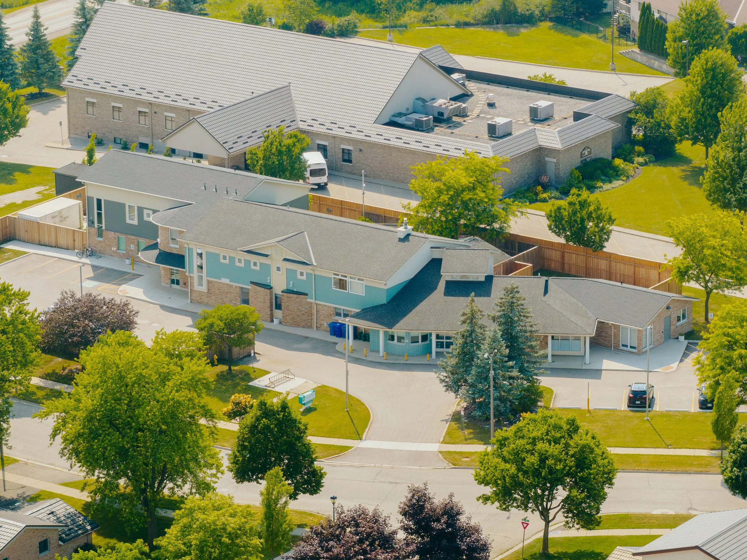 Aerial view of a residential area with modern apartments, green trees, and a parking lot.