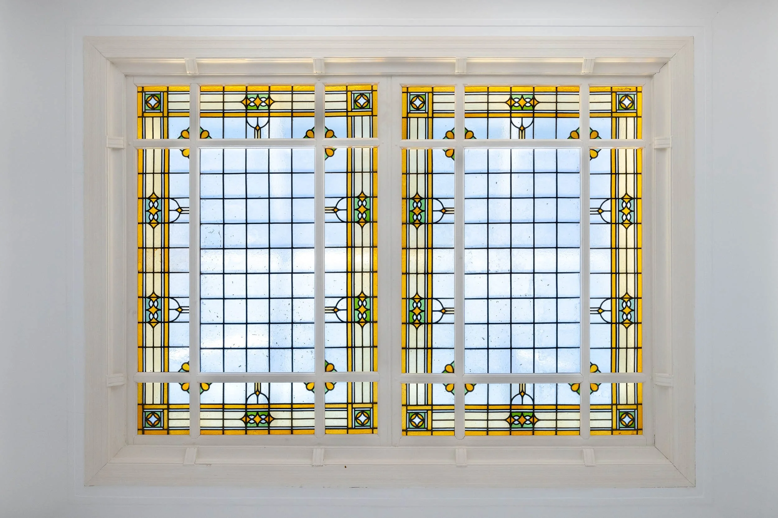 Kleurrijk glas-in-lood raampaneel met geometrisch patroon en blauwe hemel zichtbaar door het glas.