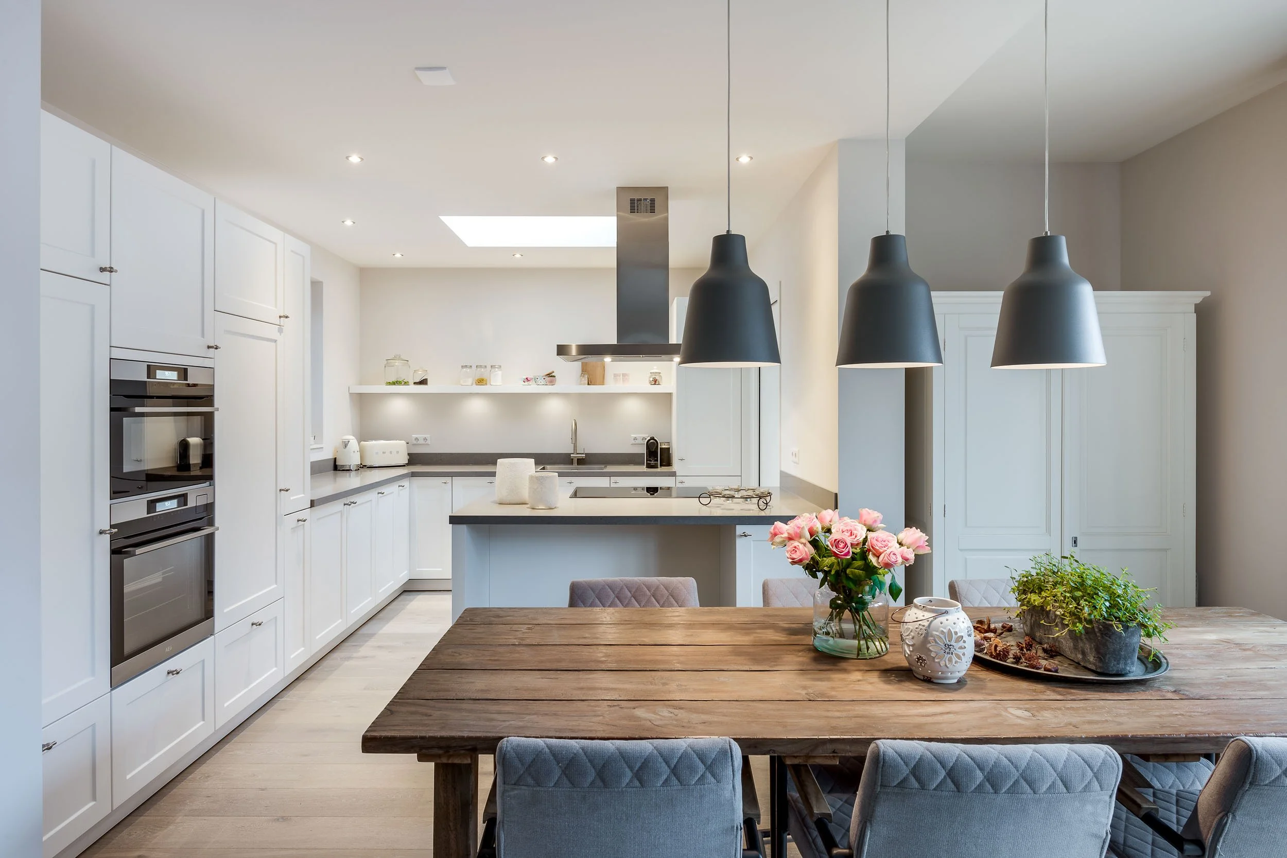 Kleine keuken met witte kasten, een eettafel met stoelen, bloemen en decoratieve items.