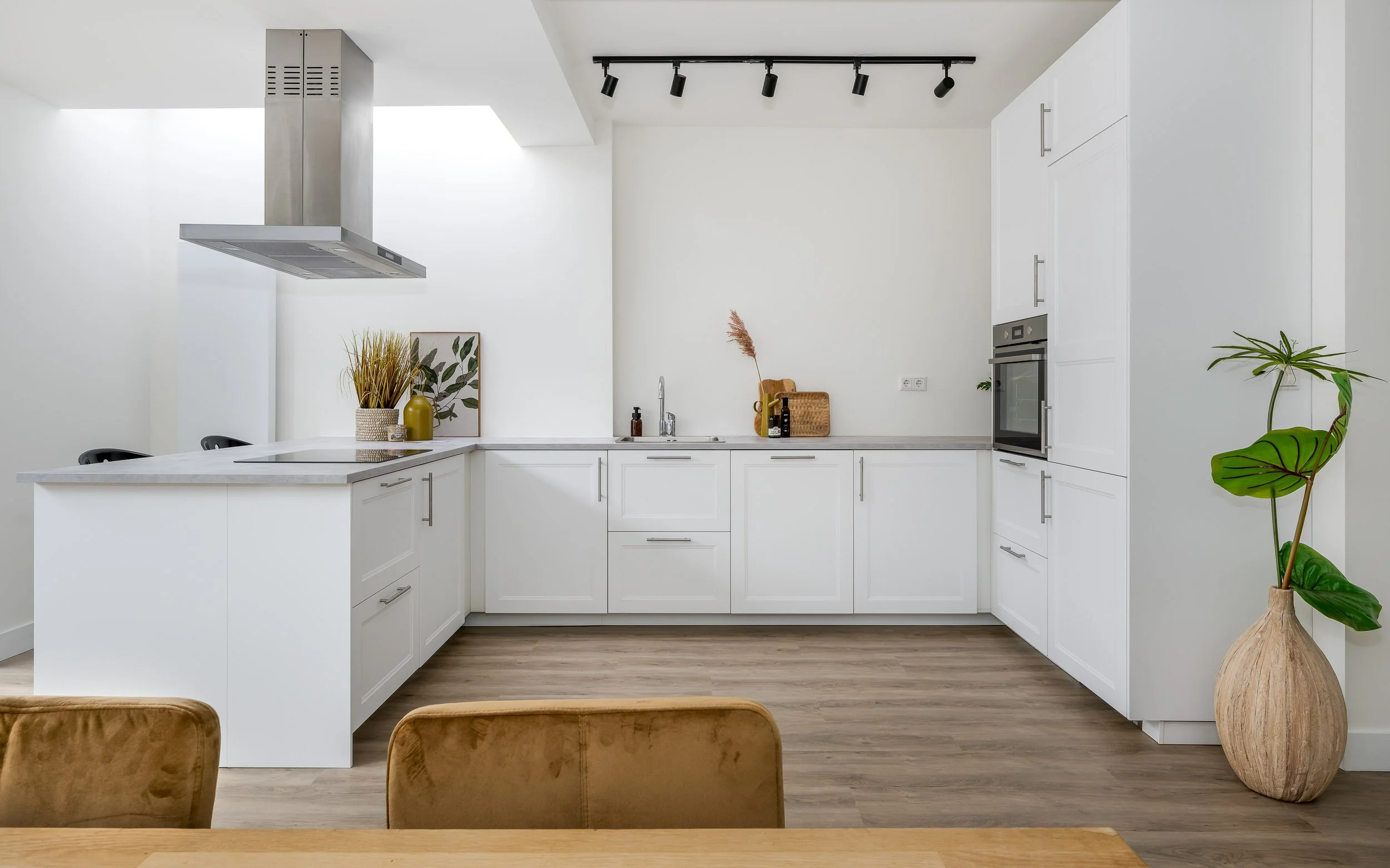 Moderne, witte keuken met veel opbergruimte, een kookeiland, planten, en natuurlijke lichtinval.