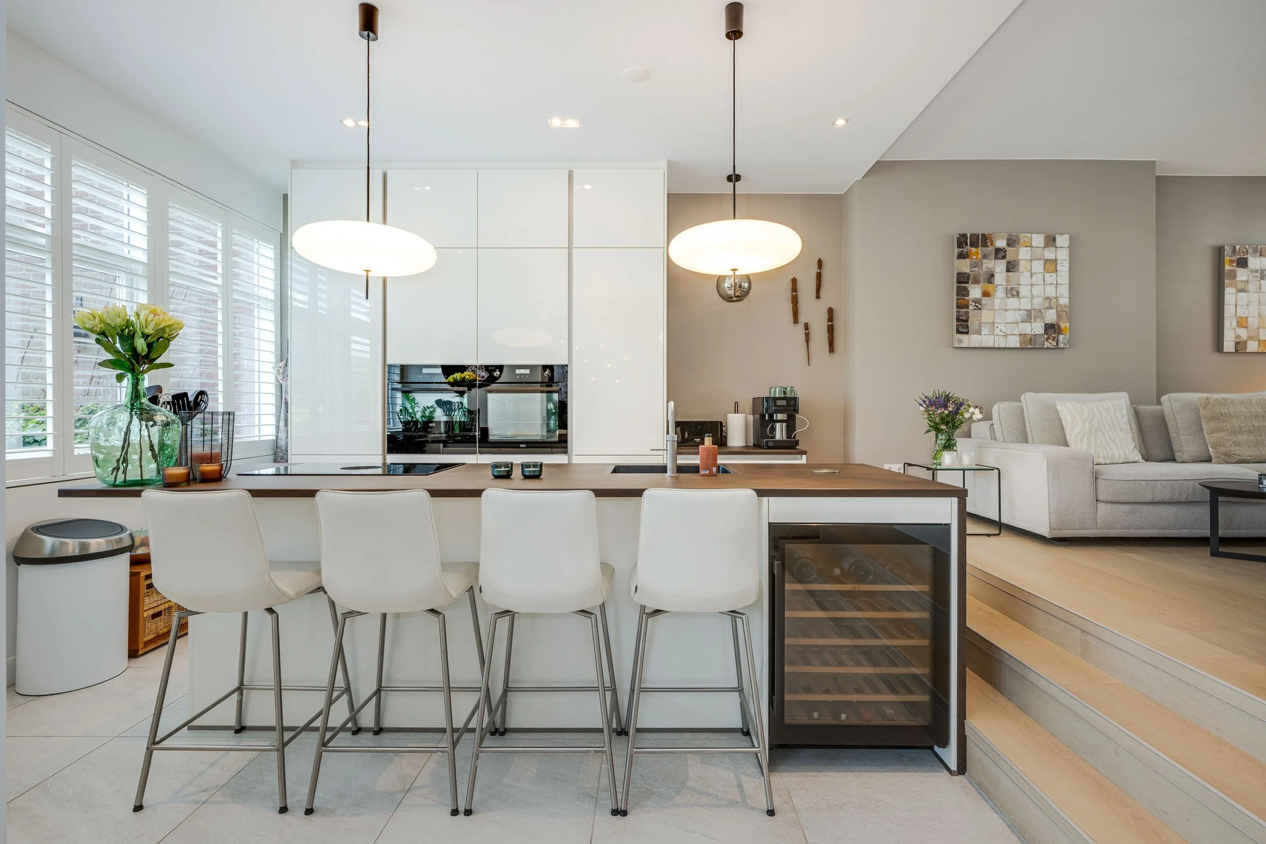 Een keuken en woonkamer met witte kasten, eettafel met witte stoelen, planten, en moderne decoraties.