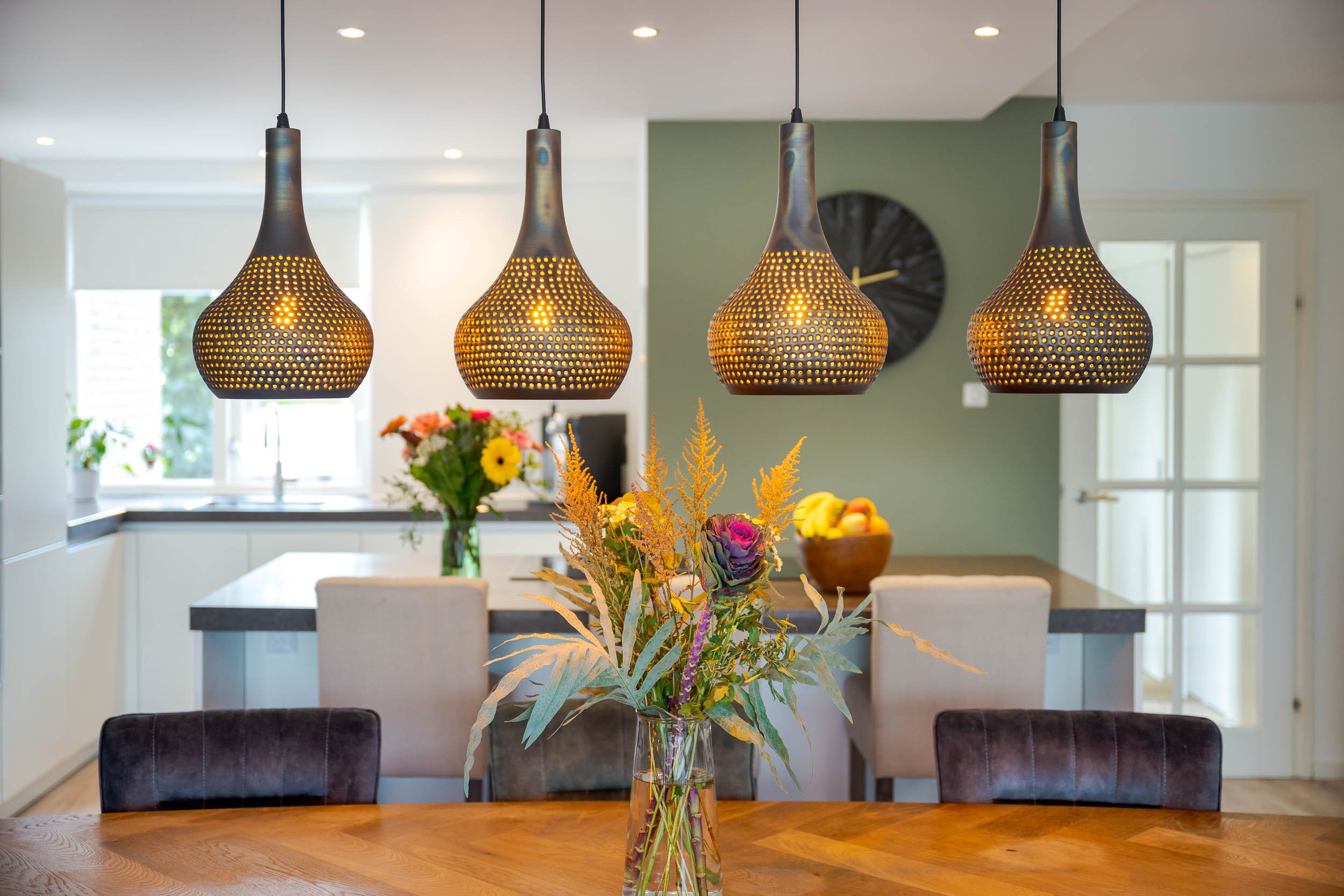 Gezicht met vier hanglampen, een tafel met een bloemenvaas en een keuken op de achtergrond