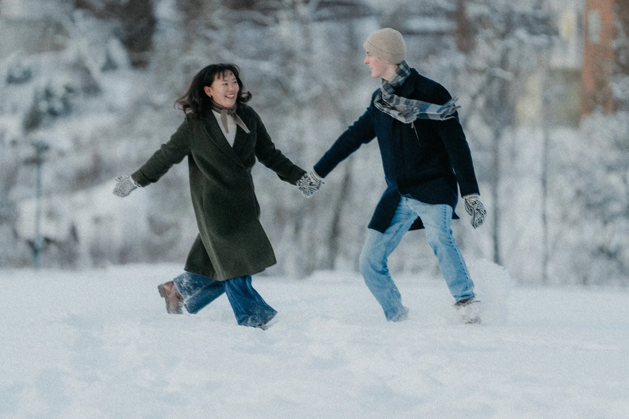 To personer løper og leker i snøen mens de holder hender og smiler.
